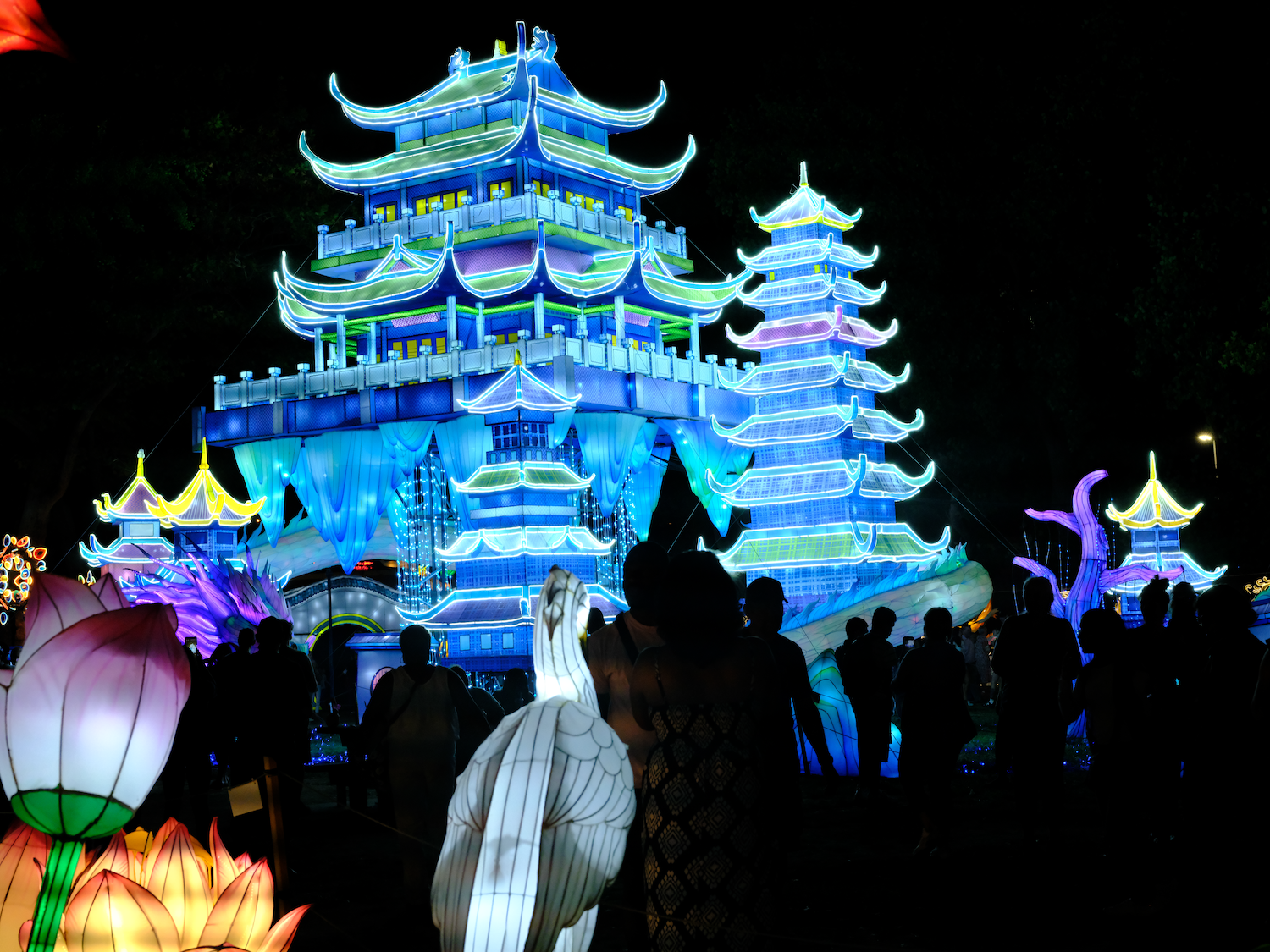 Large illuminated pagoda sculptures at night with crowds of people and colorful lights.