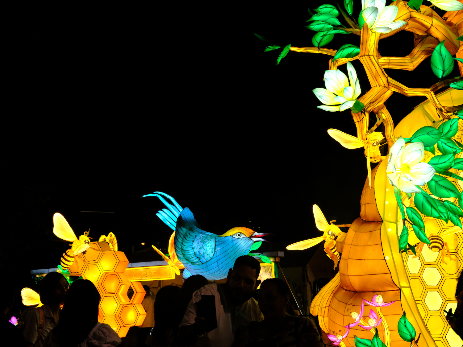 Luminous blue rooster and floral lantern with people in foreground at night.