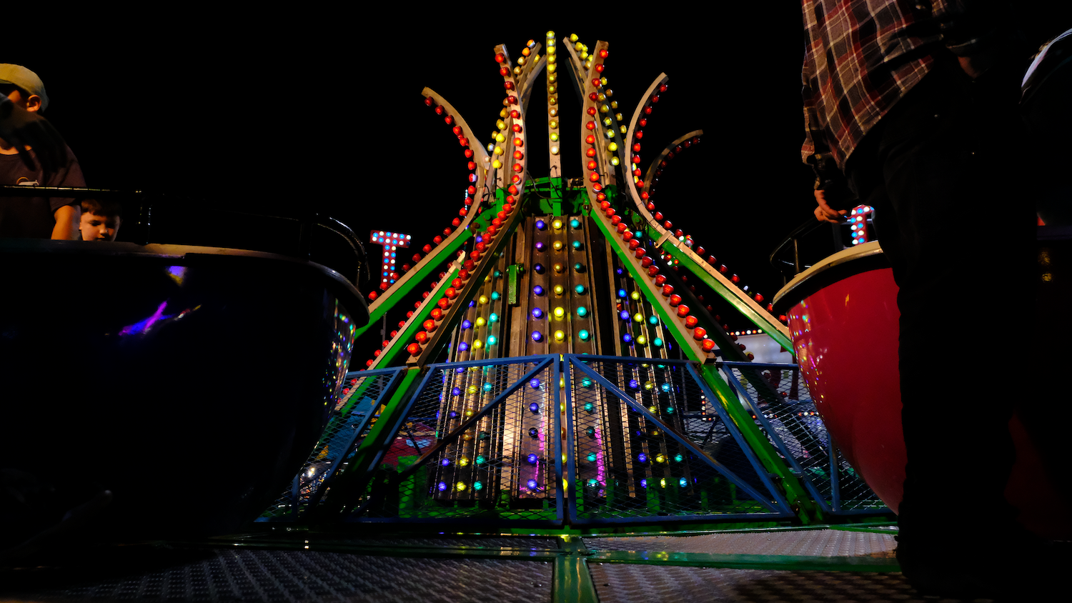 Colorful amusement park ride at night; lights and spinning cars.