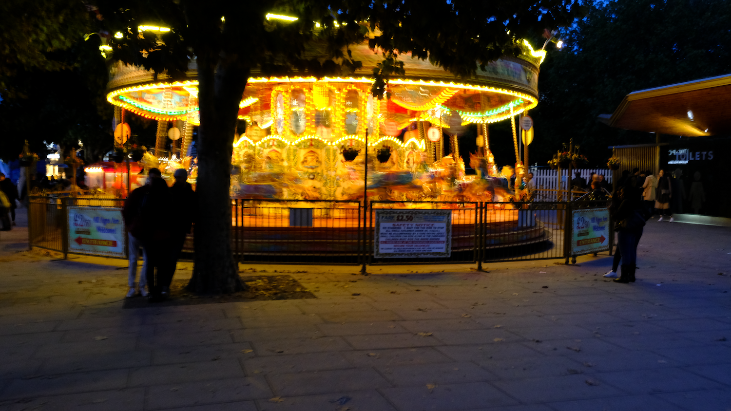 Lit-up carousel at night. People watching.