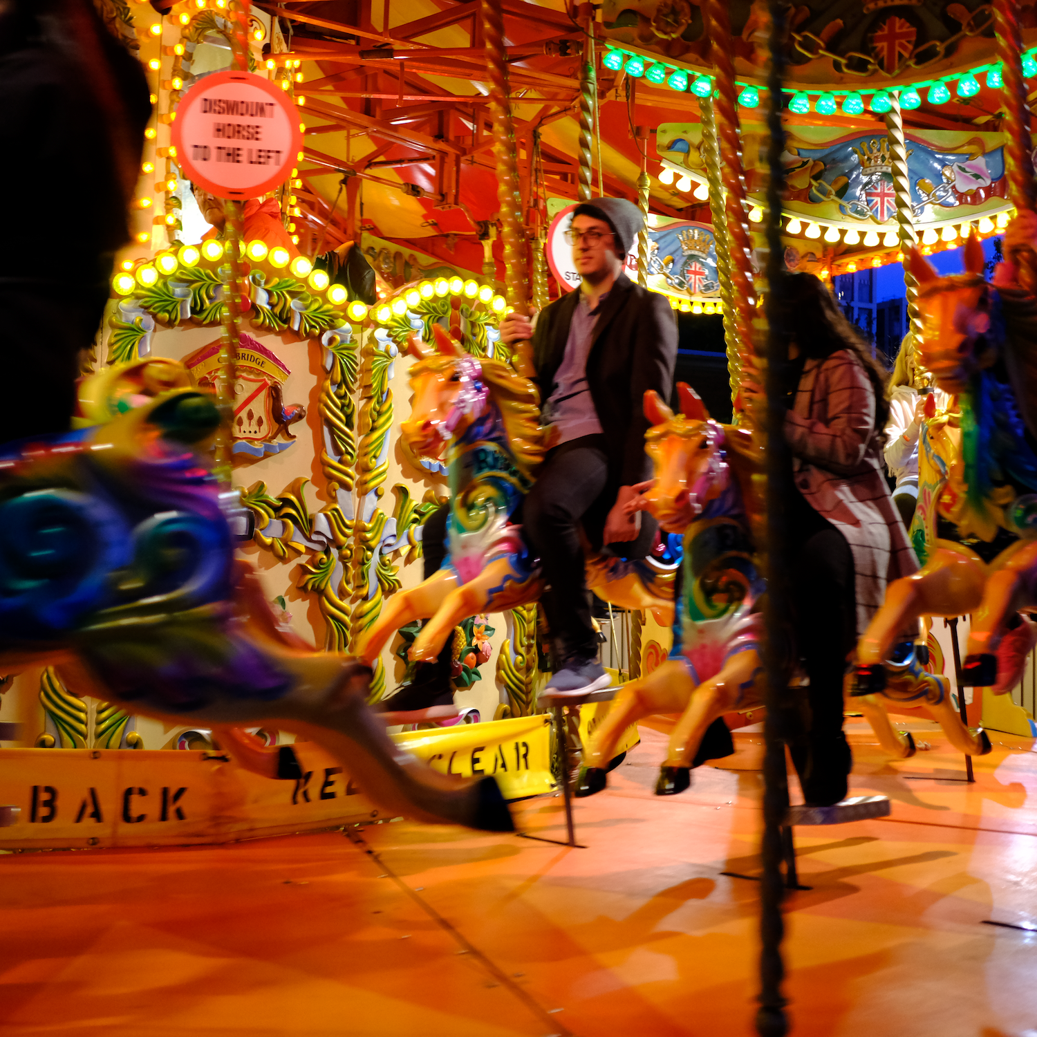 People riding a carousel with colorful horses at night, under bright lights.