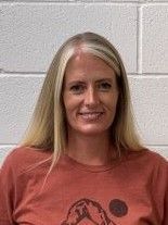 A woman in a red shirt is smiling in front of a white brick wall.