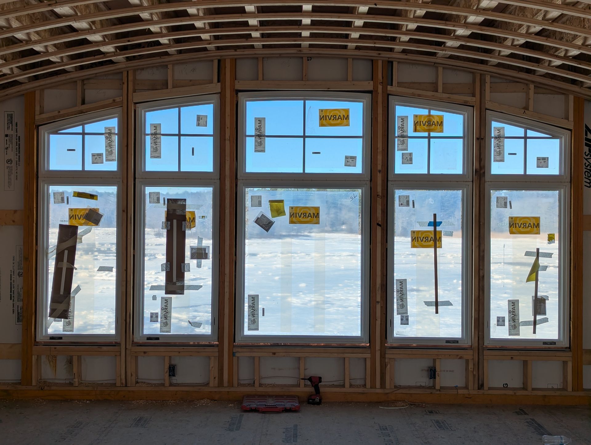 Unfinished room with large windows showing a bright snowy landscape outside.