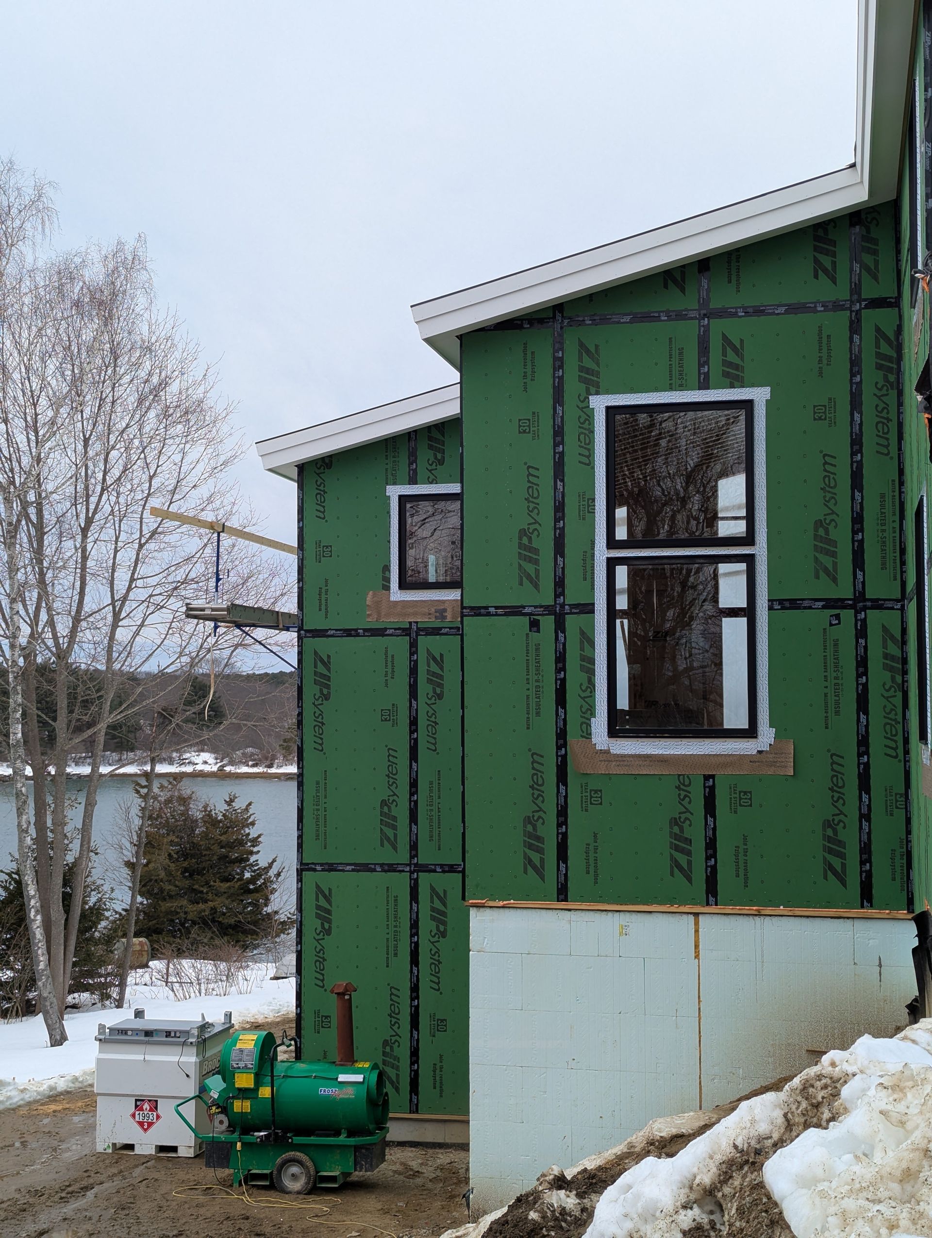 Green house under construction beside a snowy yard with a generator and propane tank outside