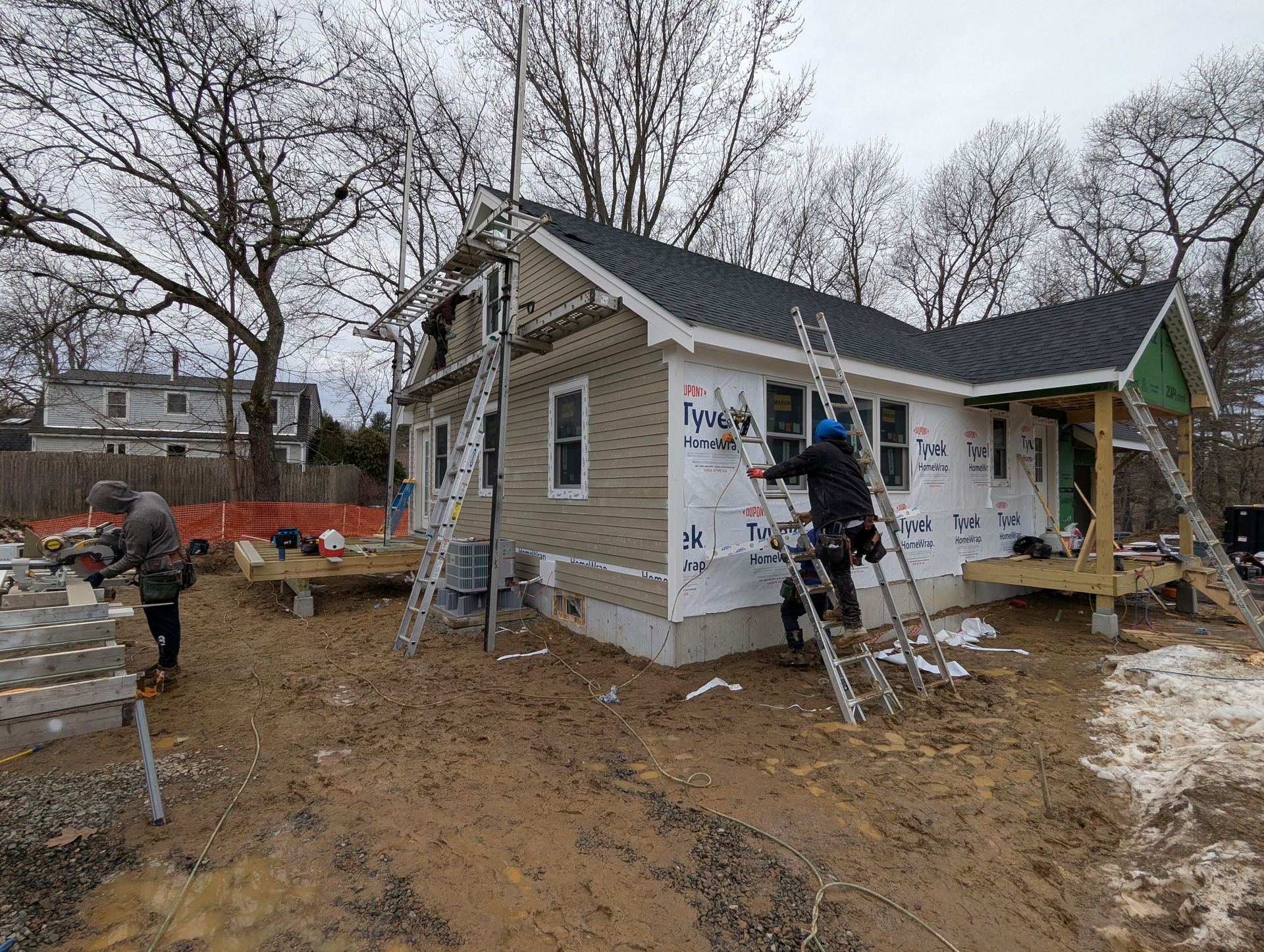Workers repairing a damaged house with ladders and scaffolding in a muddy yard