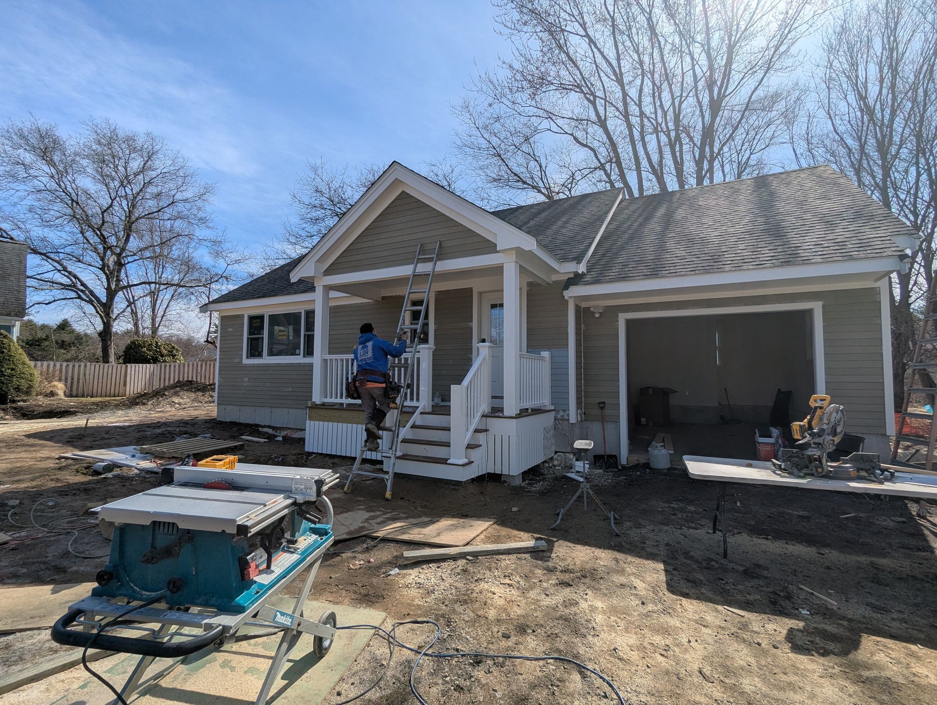House exterior under renovation with worker on porch and open garage, construction equipment in front