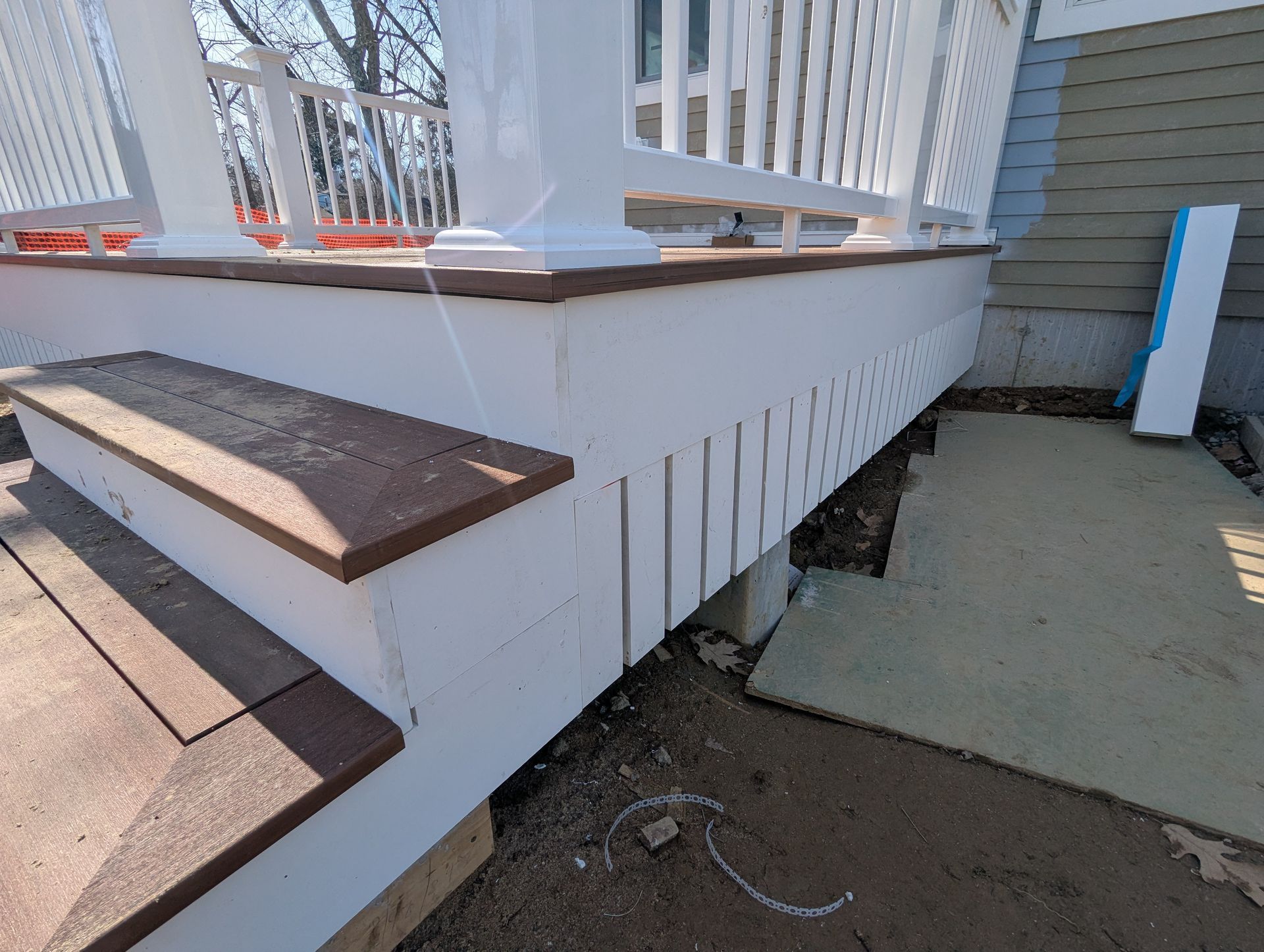 White porch steps with brown treads beside a house, showing damage and debris under the railing