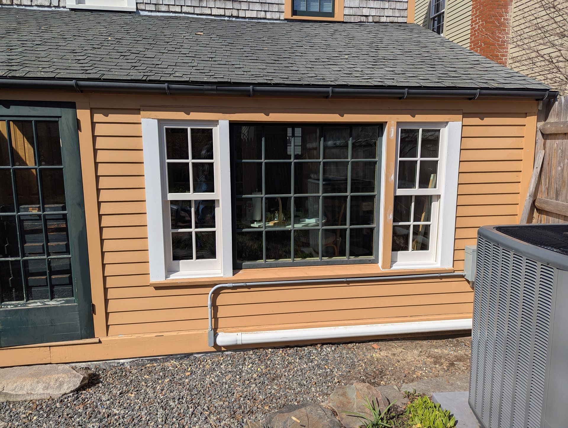 Tan house exterior with white-trimmed windows and a black door, beside a gravel path.