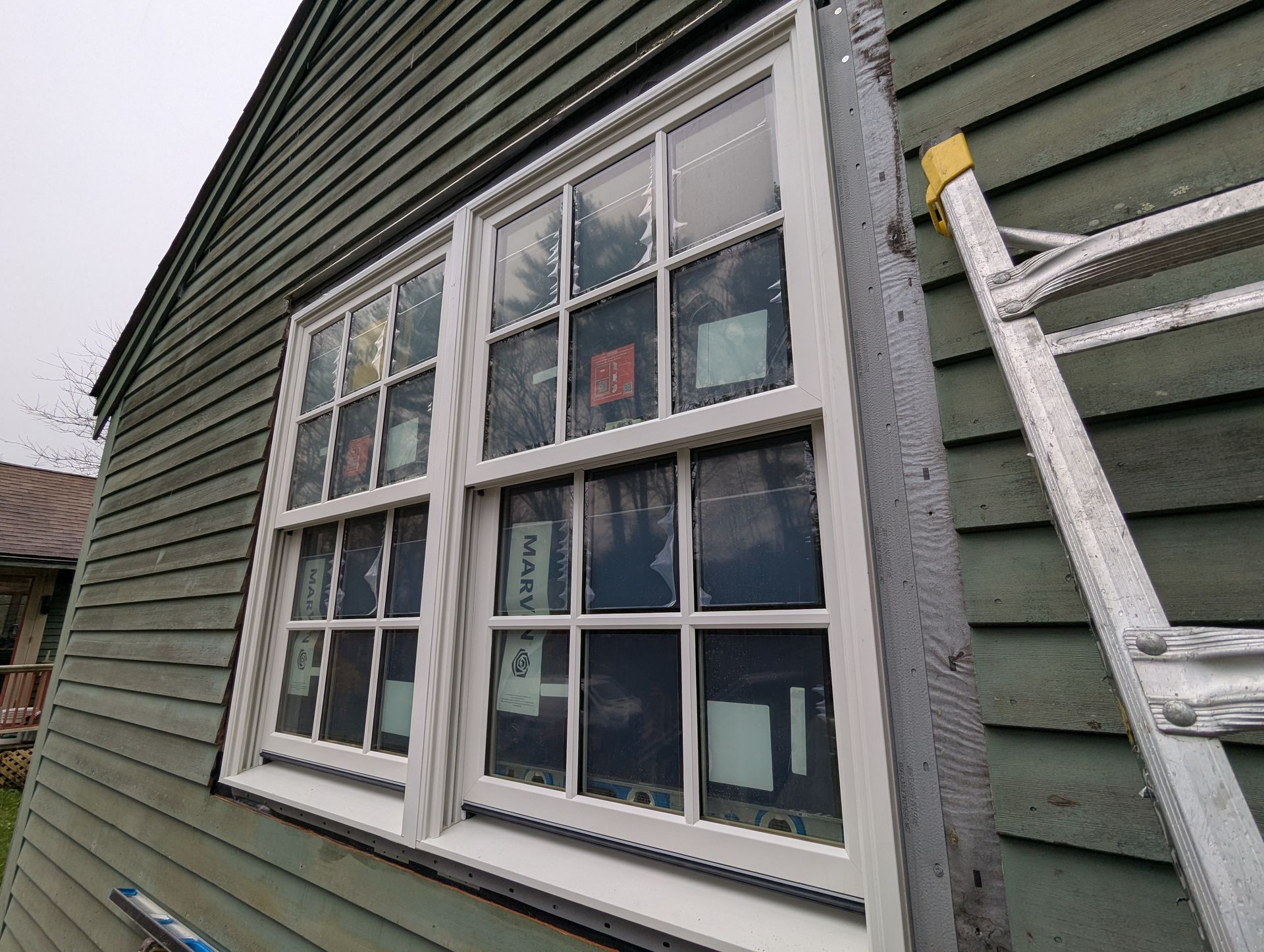 White-paned window on green house siding with a ladder leaning beside it