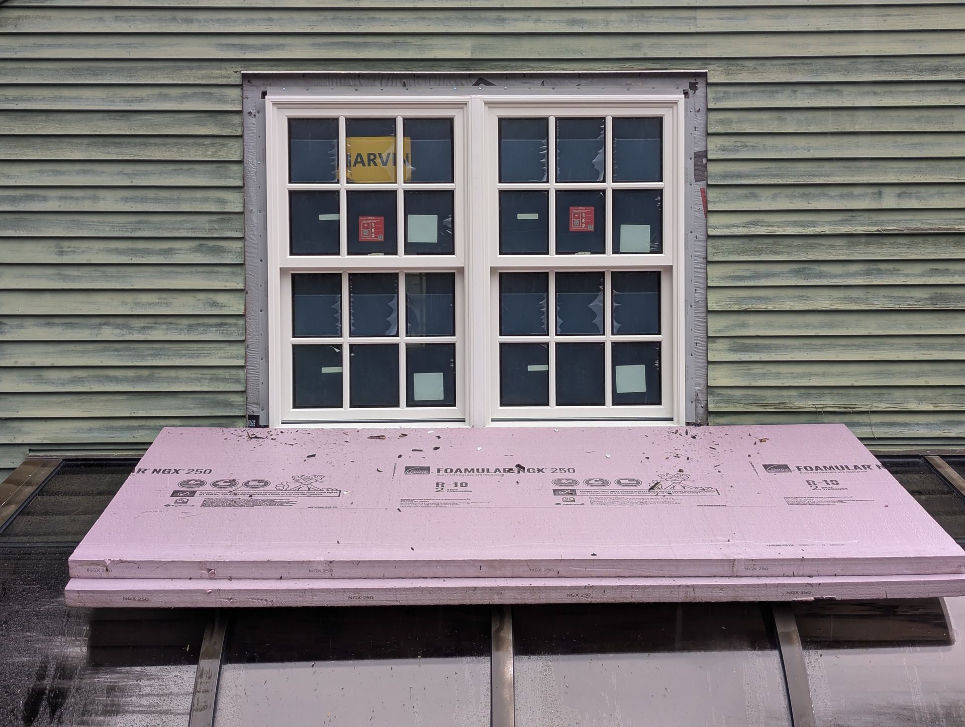 Pink informational sign beneath a window on a weathered green building wall