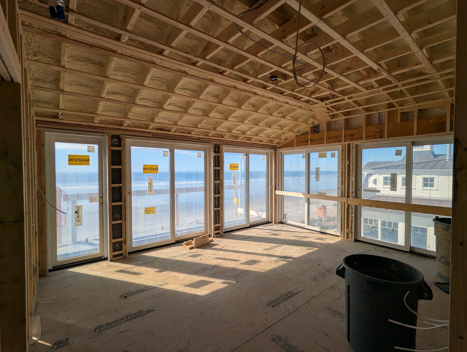Unfinished room with exposed wood framing, many windows, and a black bucket on the floor overlooking water.
