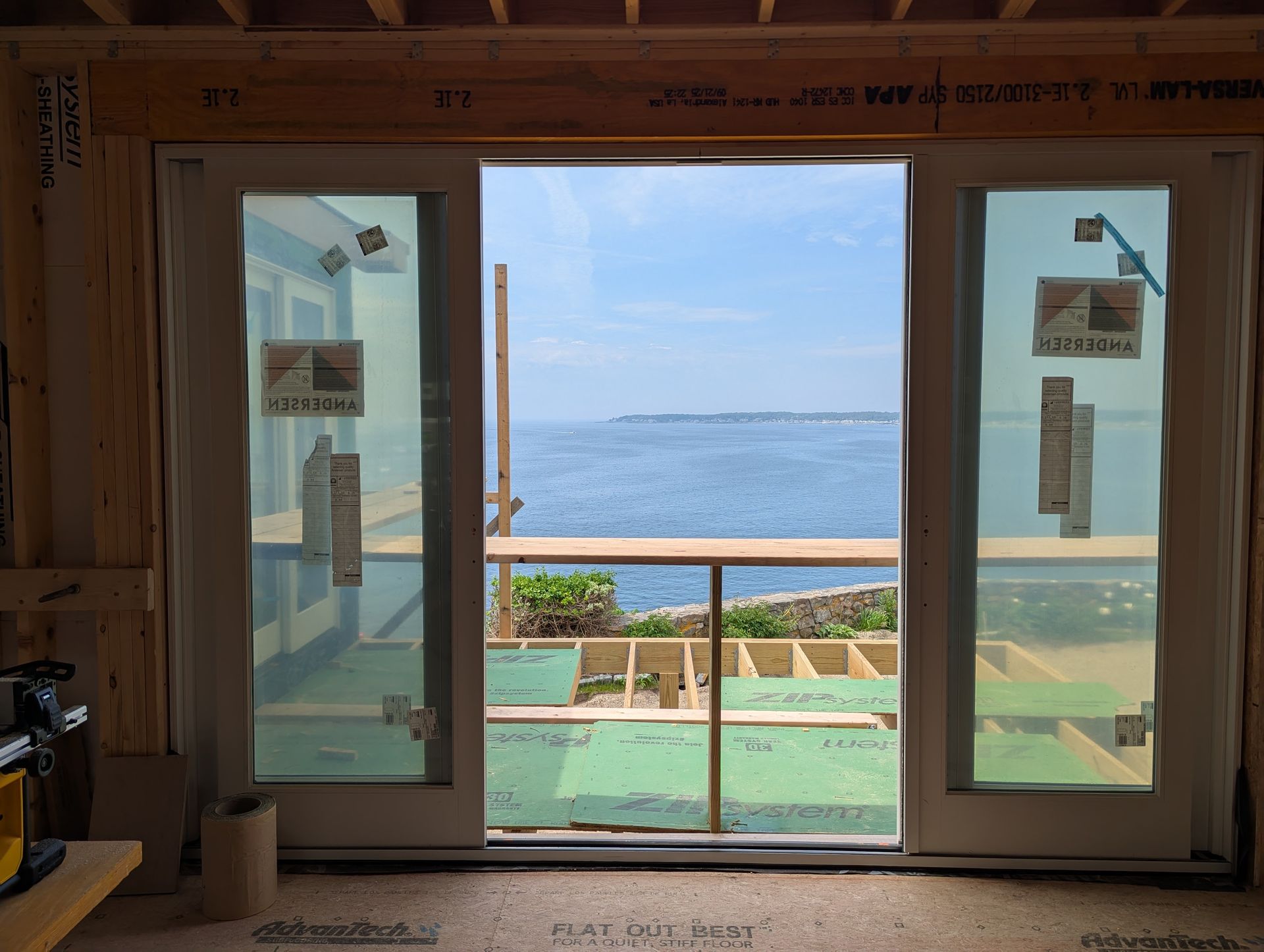 Sliding glass doors open to a sunlit ocean view from inside a rustic room.