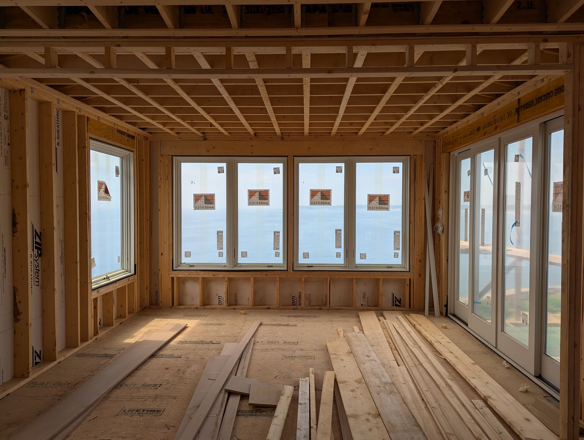 Unfinished wooden room interior with exposed framing and large windows letting in daylight.