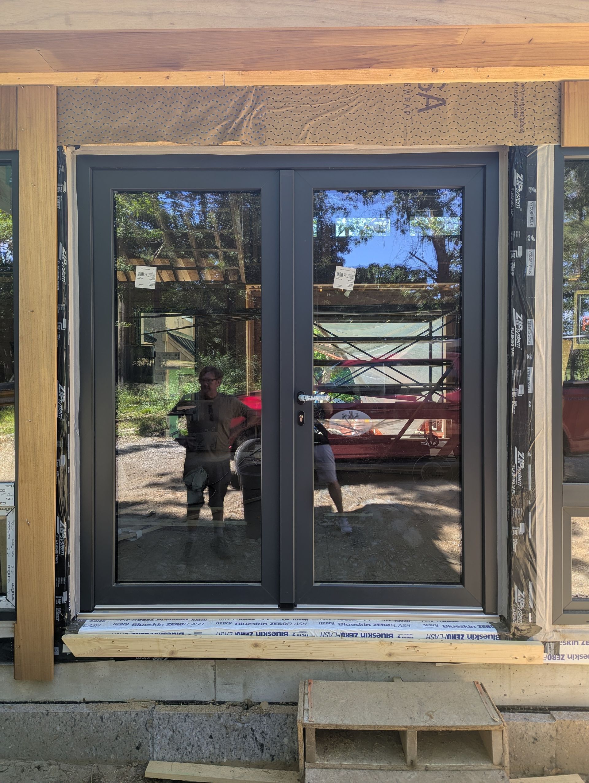 Sliding glass doors in a wooden frame at a house exterior, with reflections of a yard and truck.