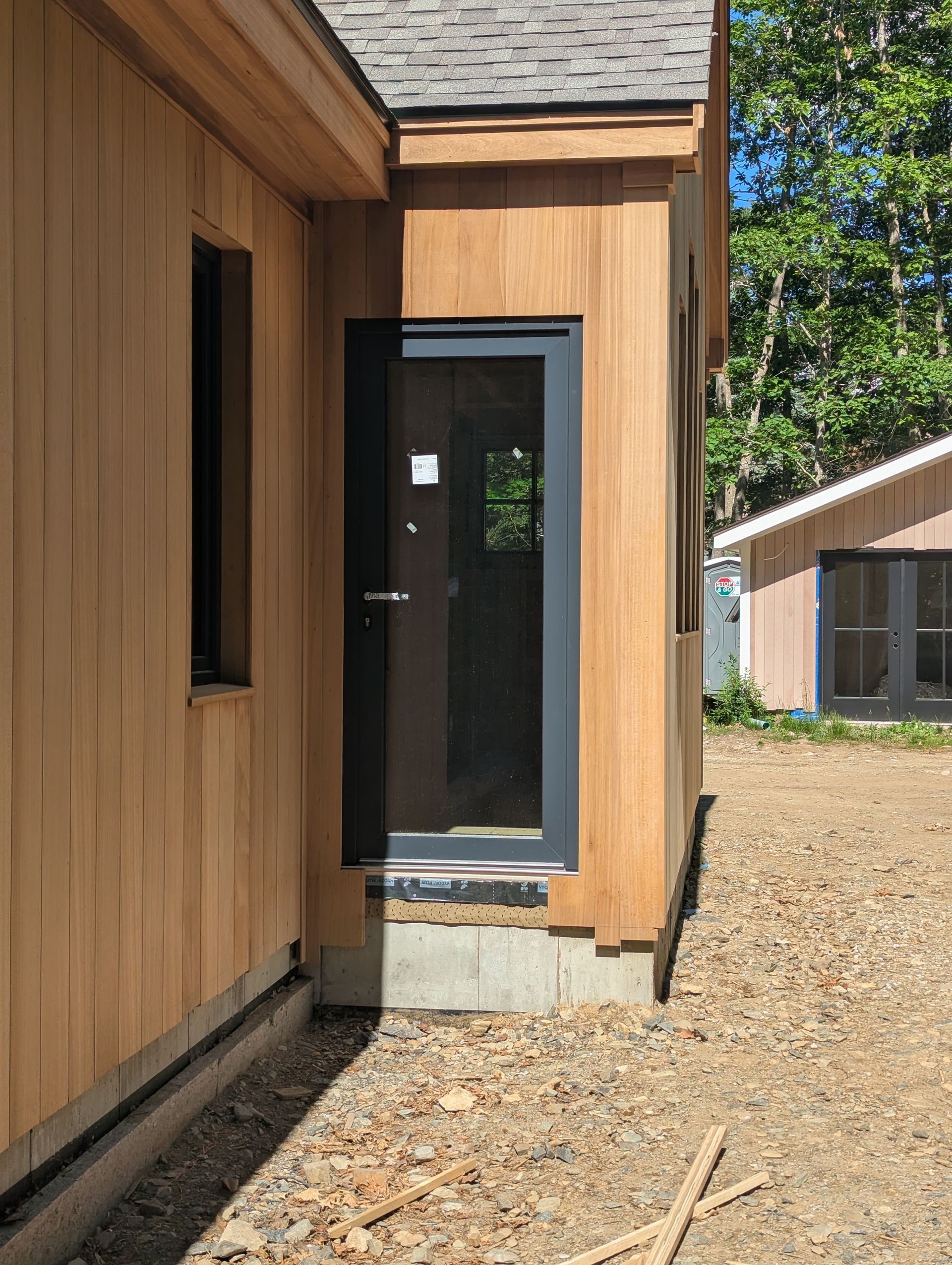 Modern house entryway with wood siding, a black-framed glass door, and gravel path.