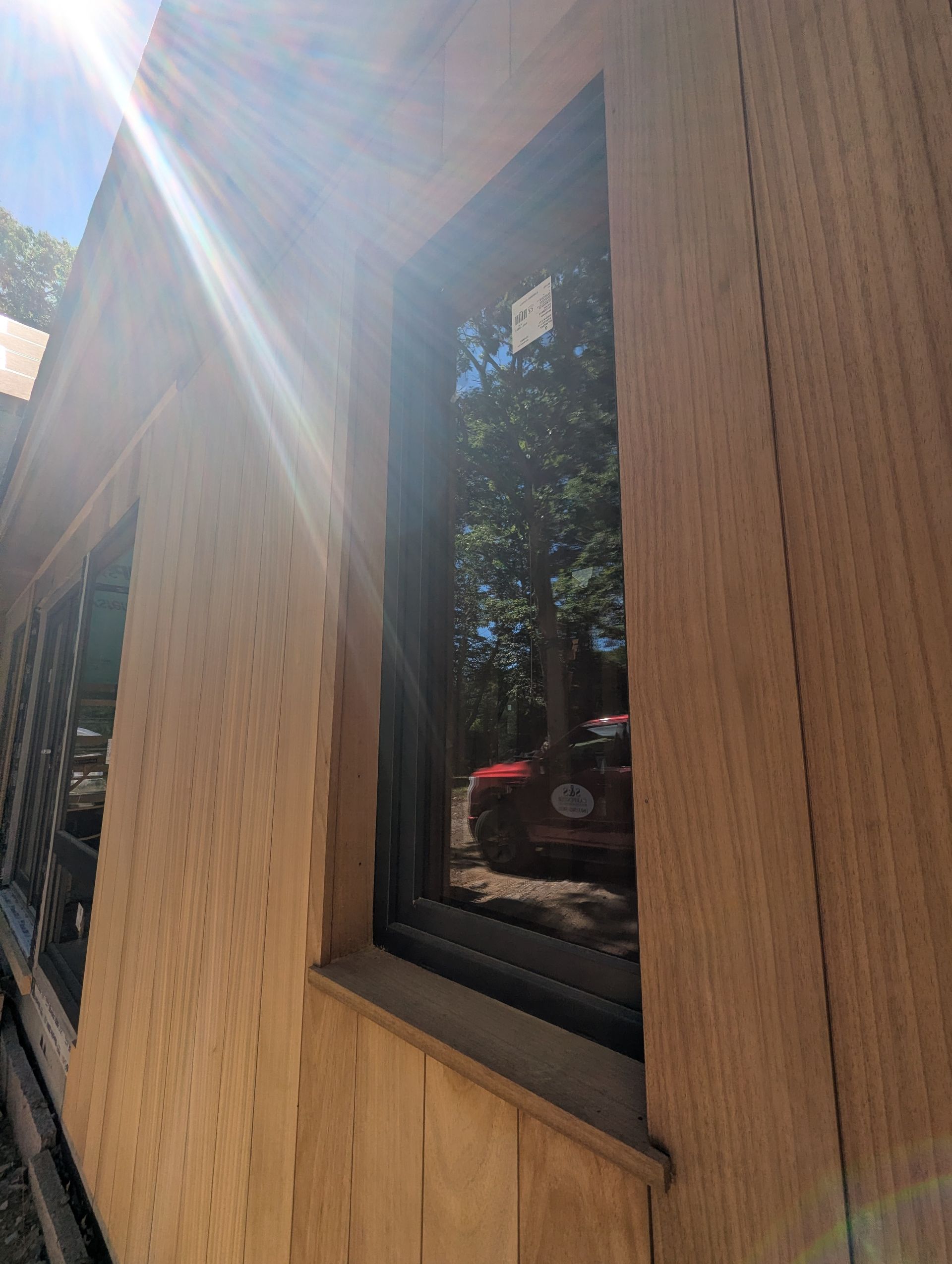 Wooden exterior wall with a narrow window reflecting trees and sunlight glare