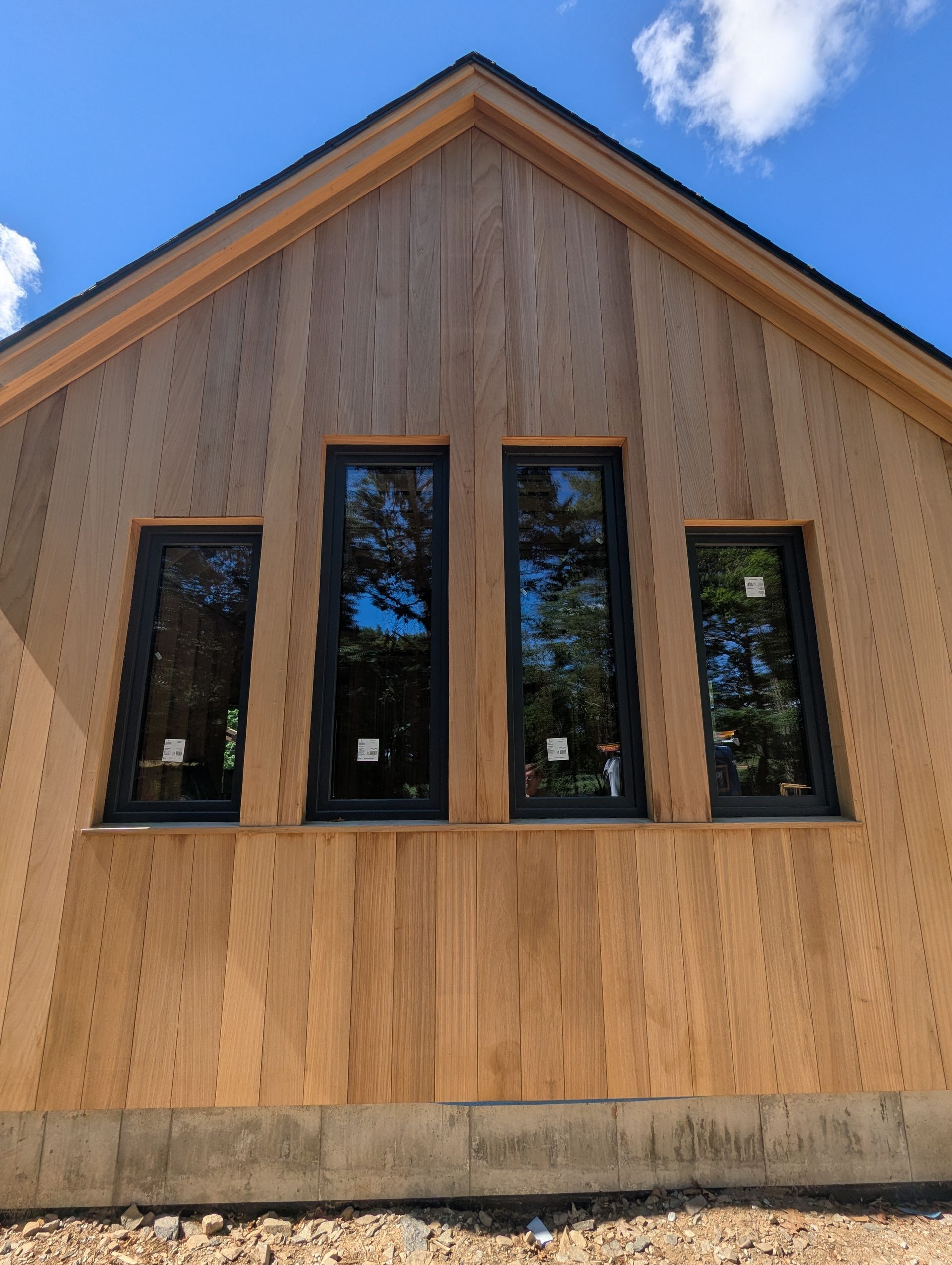 Wooden building facade with four tall black-framed windows under a peaked roof