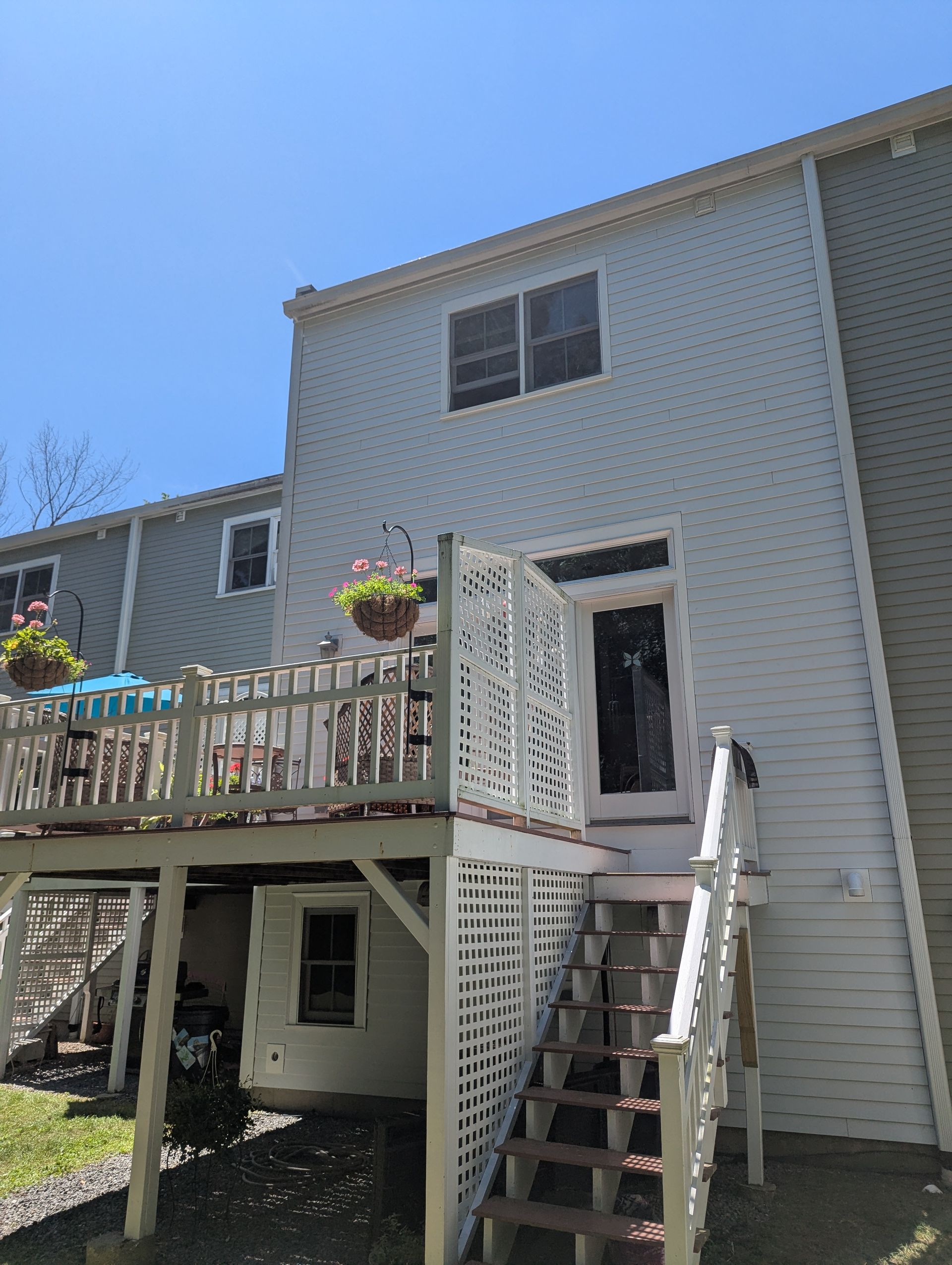 Backyard deck with stairs leading to a white house, hanging flower baskets, and a bright blue sky.