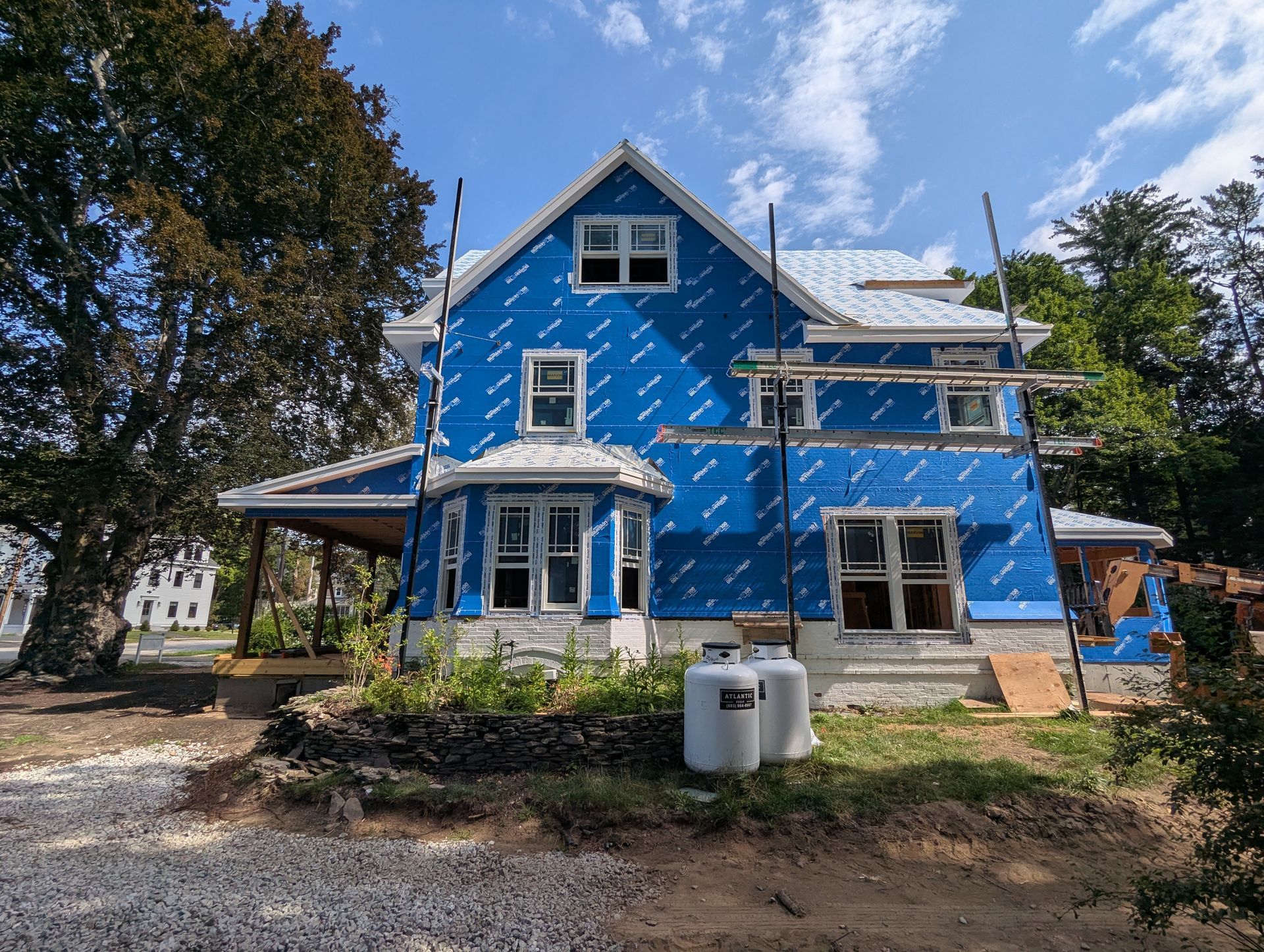 Blue house under construction with white trim, scaffolding, and trees in the yard