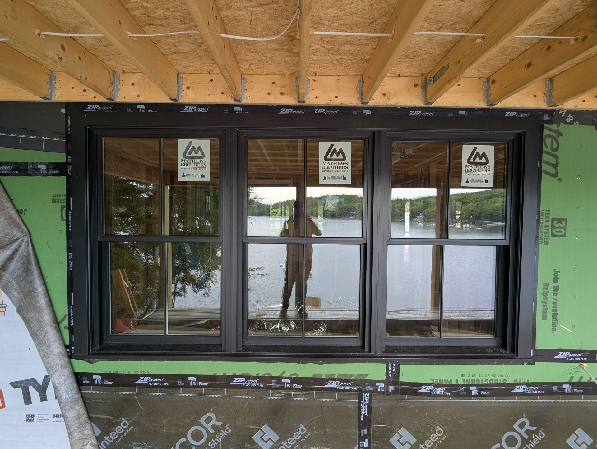 Black-framed window under construction in a wall opening with green insulation and exposed wooden framing