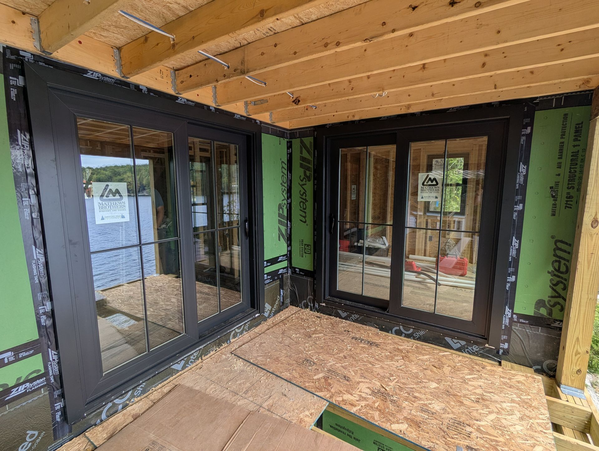 Interior of a building under construction with black-framed sliding glass doors and exposed wood ceiling.