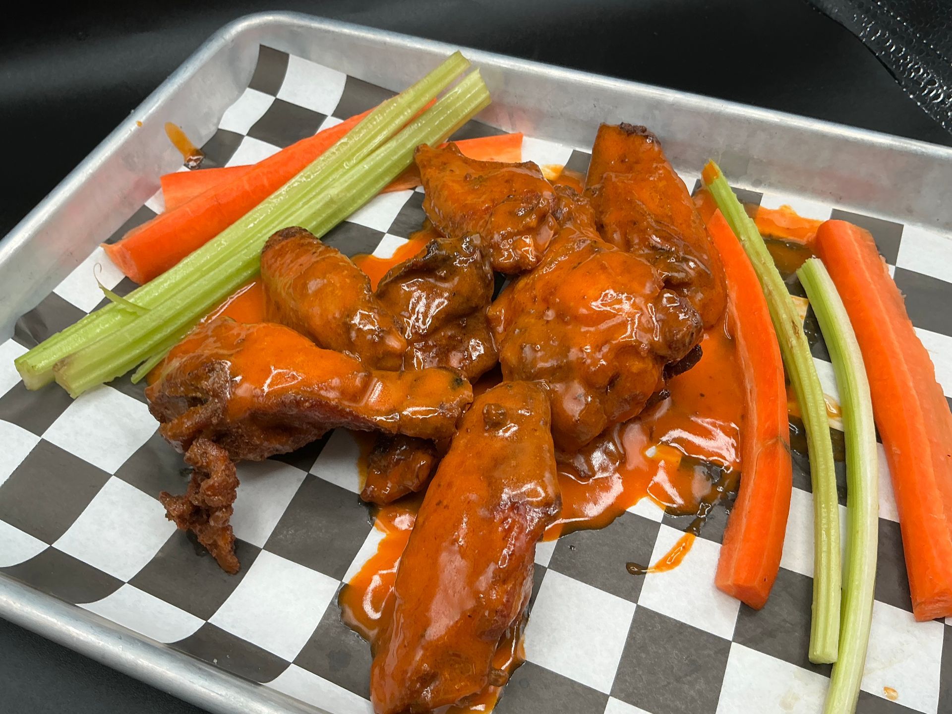 Buffalo wings with carrots and celery on a checkered tray.