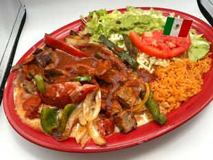 Plate of Mexican food: steak, peppers, rice, lettuce, guacamole, tomato, and a Mexican flag.