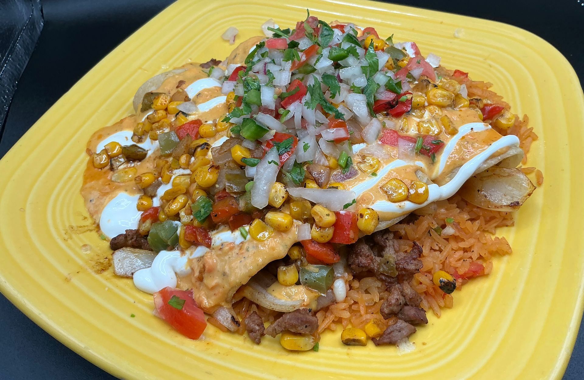 Yellow plate of Mexican food: rice, meat, grilled corn, white sauce, and pico de gallo.