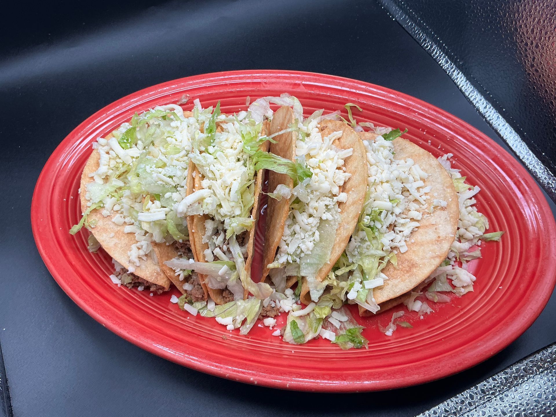 Three tacos on a red plate, topped with shredded lettuce and cheese.