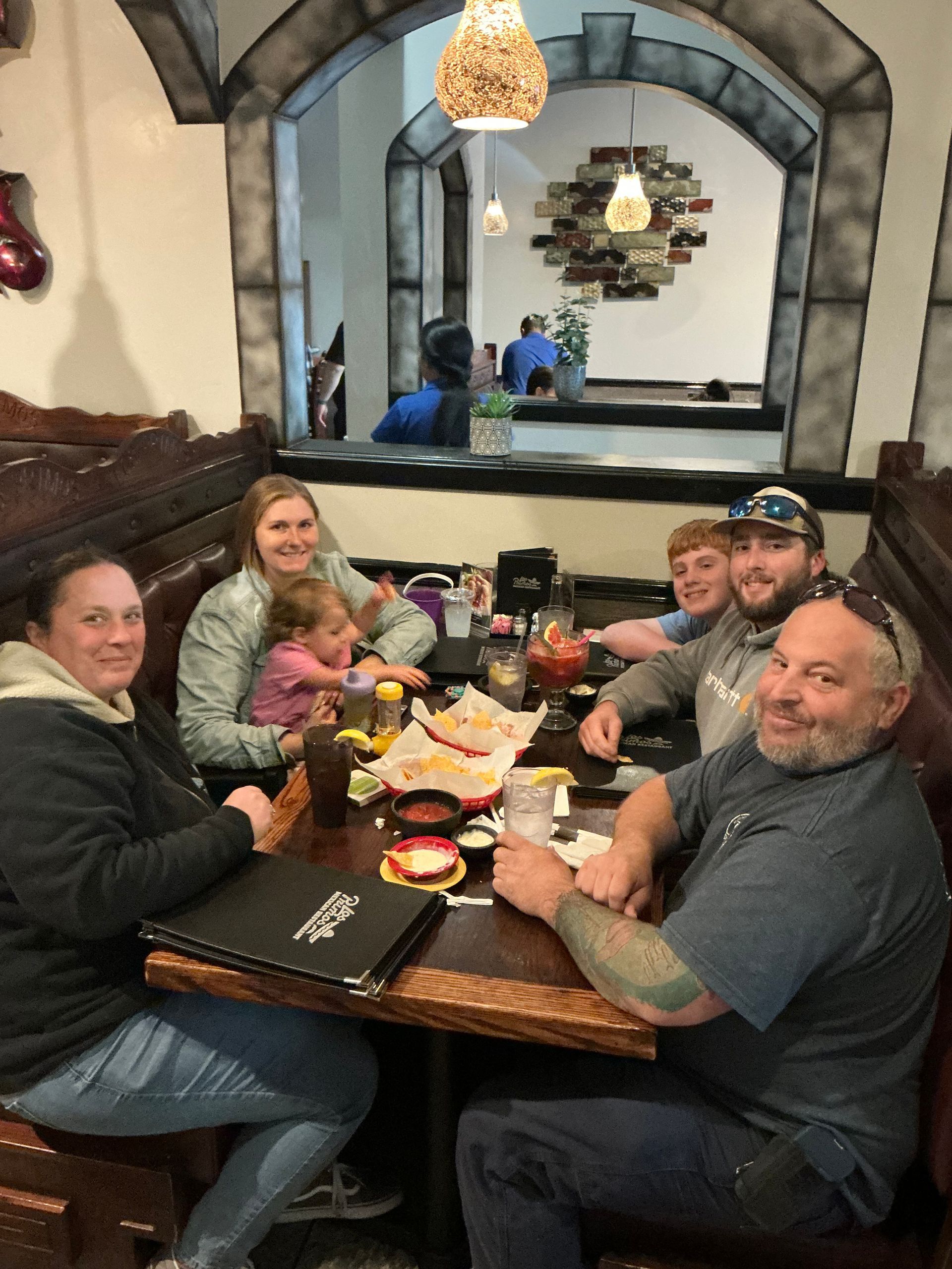 People at a table in a restaurant. They are smiling and eating. Tortilla chips are on the table.
