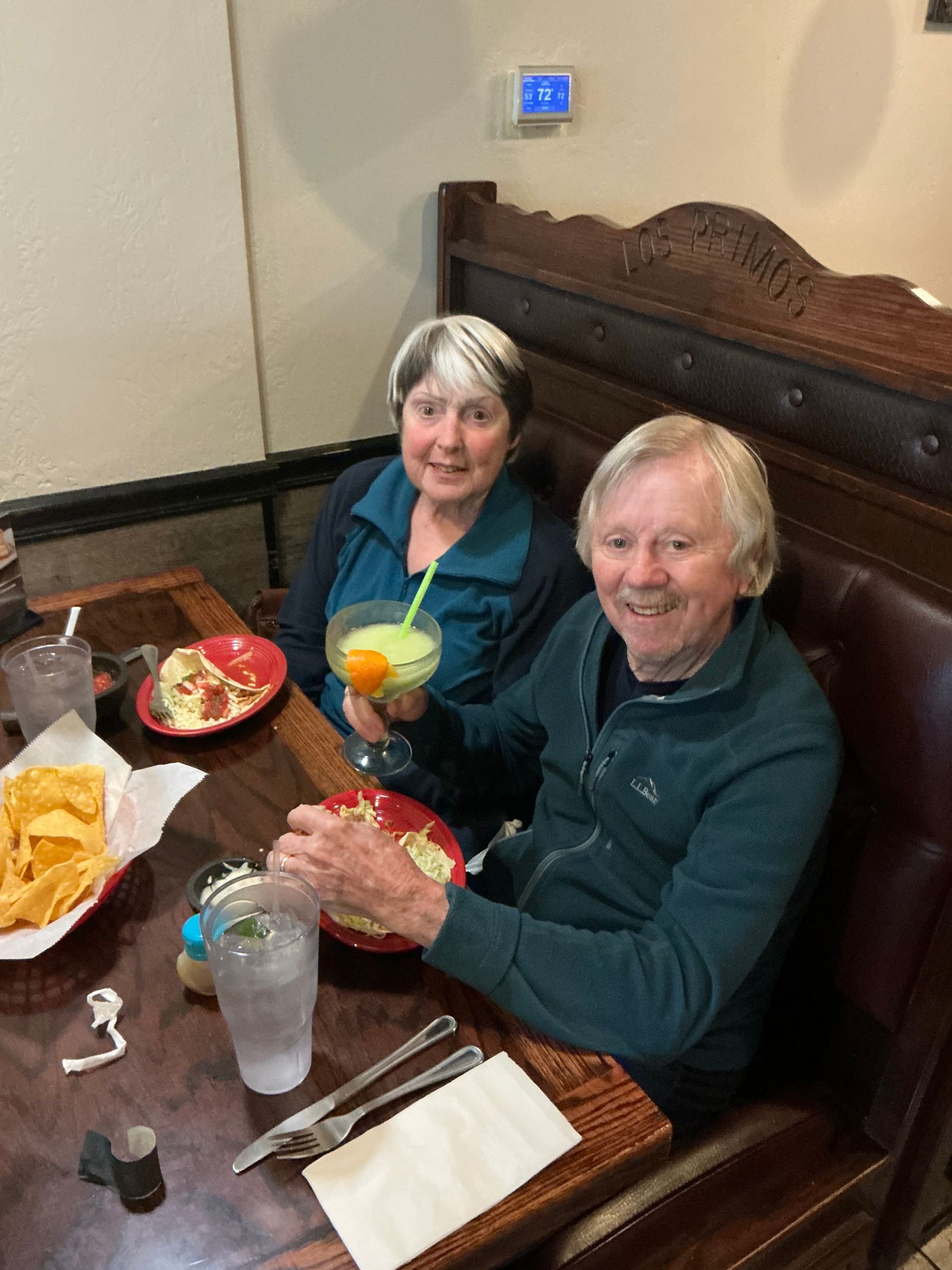 Two people at a restaurant table with food and drinks. The person on the right is smiling.