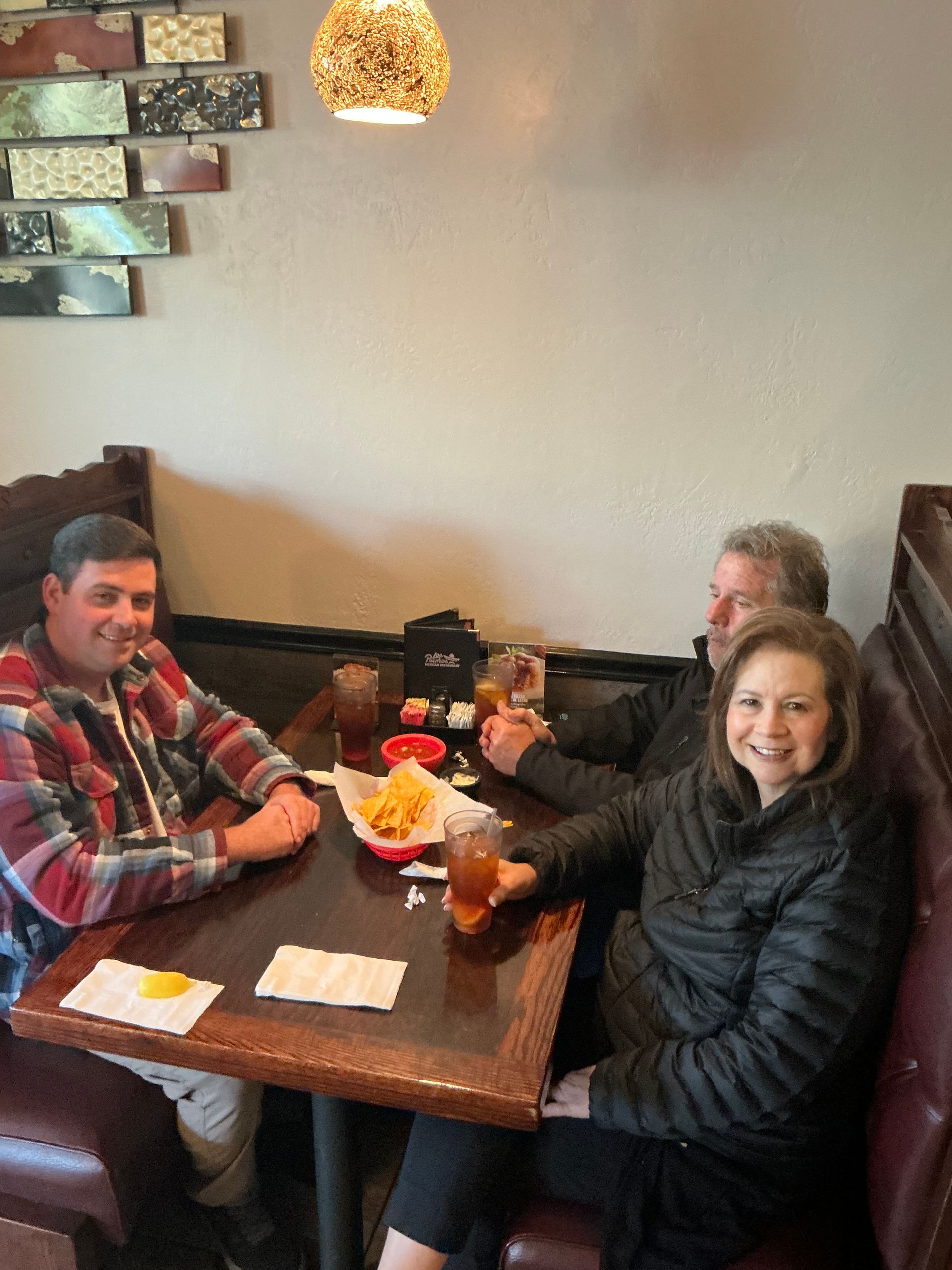 Three people seated at a table in a restaurant; one smiles and holds a drink.
