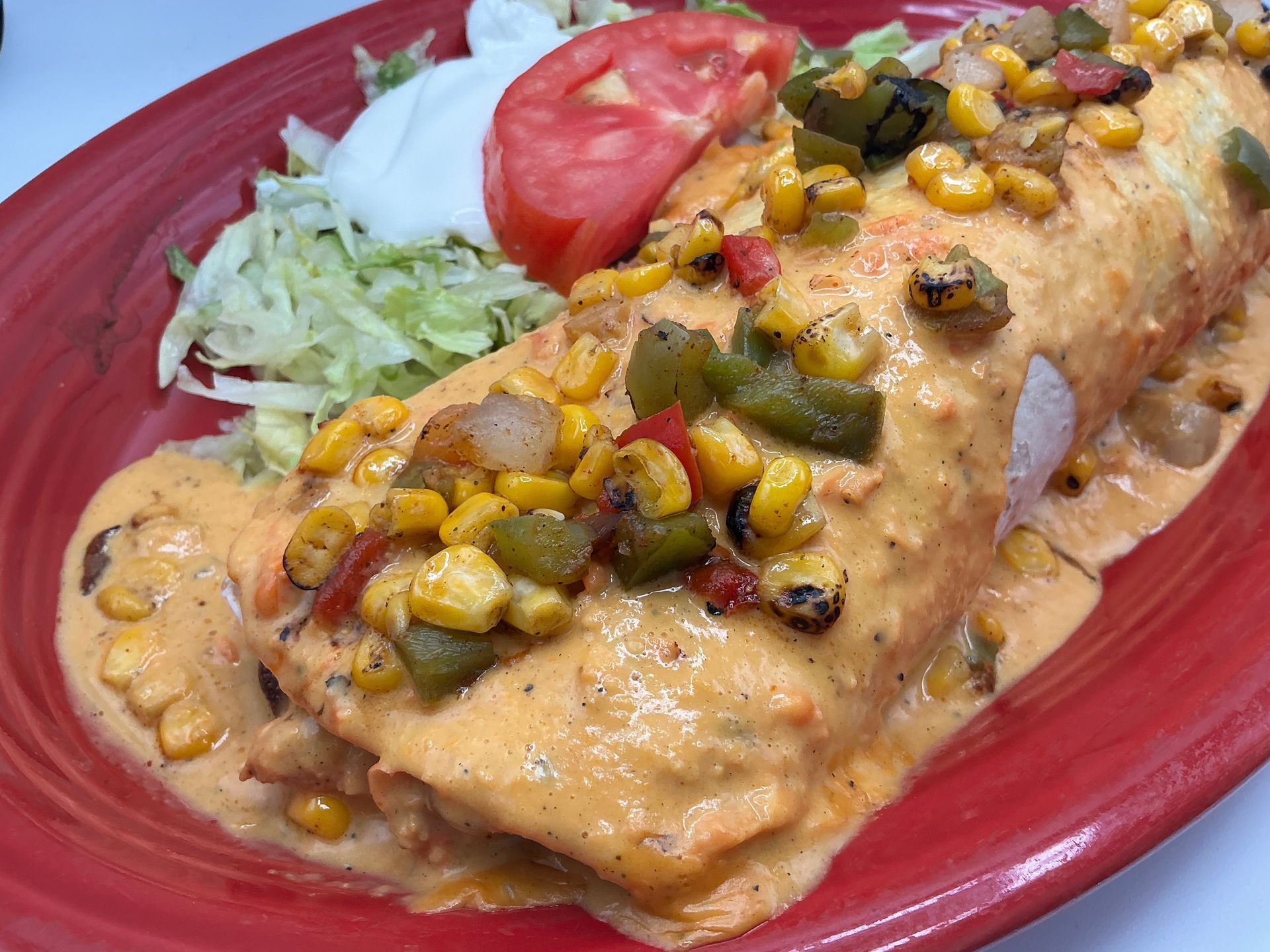 Burrito covered in creamy orange sauce, topped with corn and peppers, served with lettuce, tomato, and sour cream.