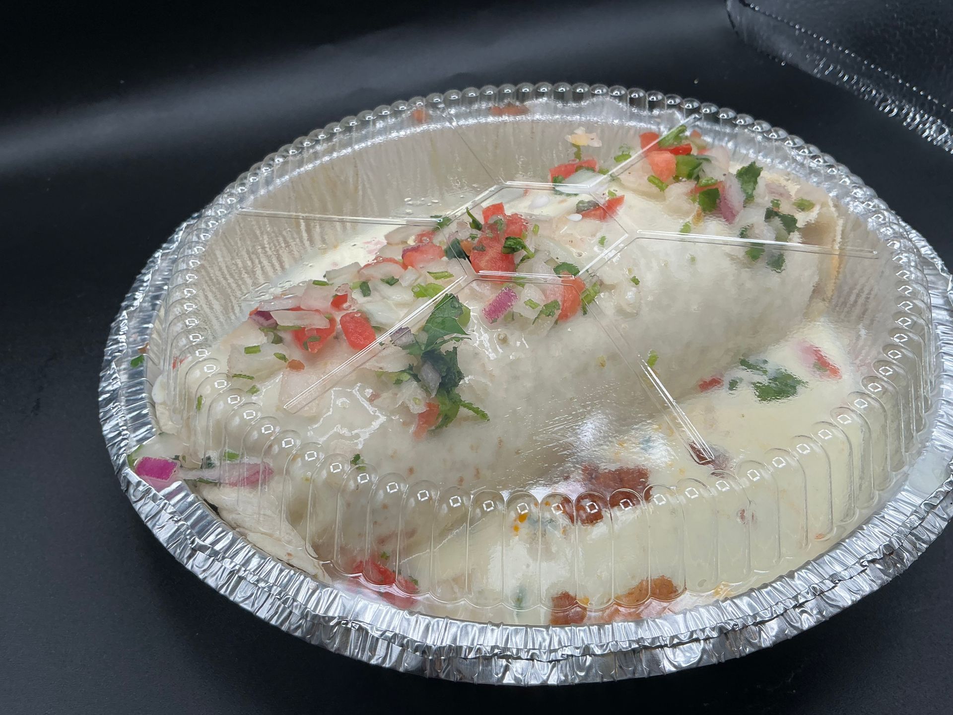 Burrito in a foil container, covered in white sauce and salsa.