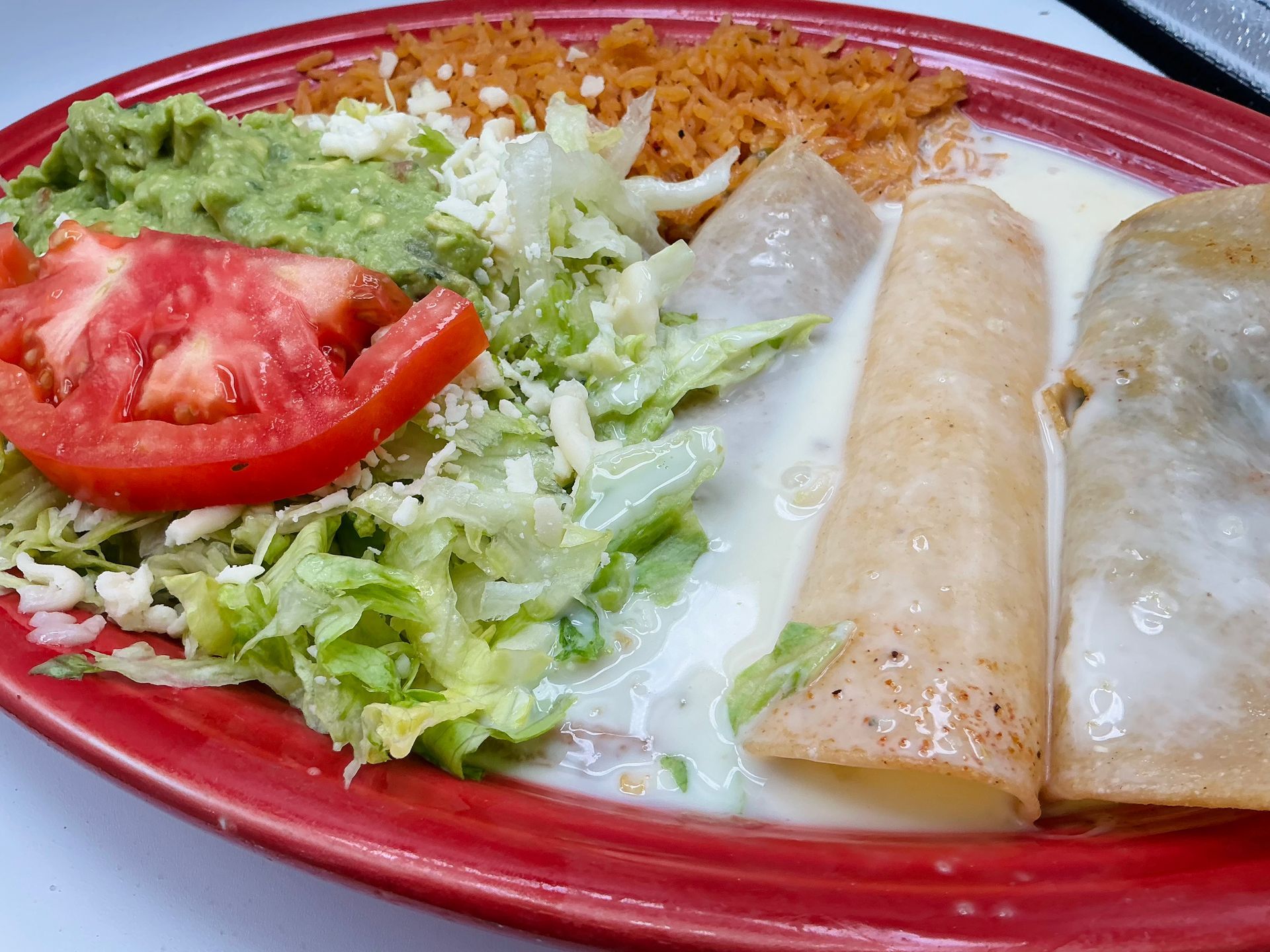 Plate of Mexican food: enchiladas, rice, guacamole, tomato, lettuce.