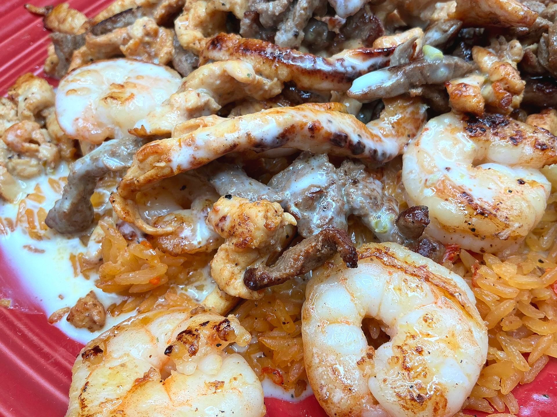 Grilled shrimp, chicken, and beef over rice in a red container.