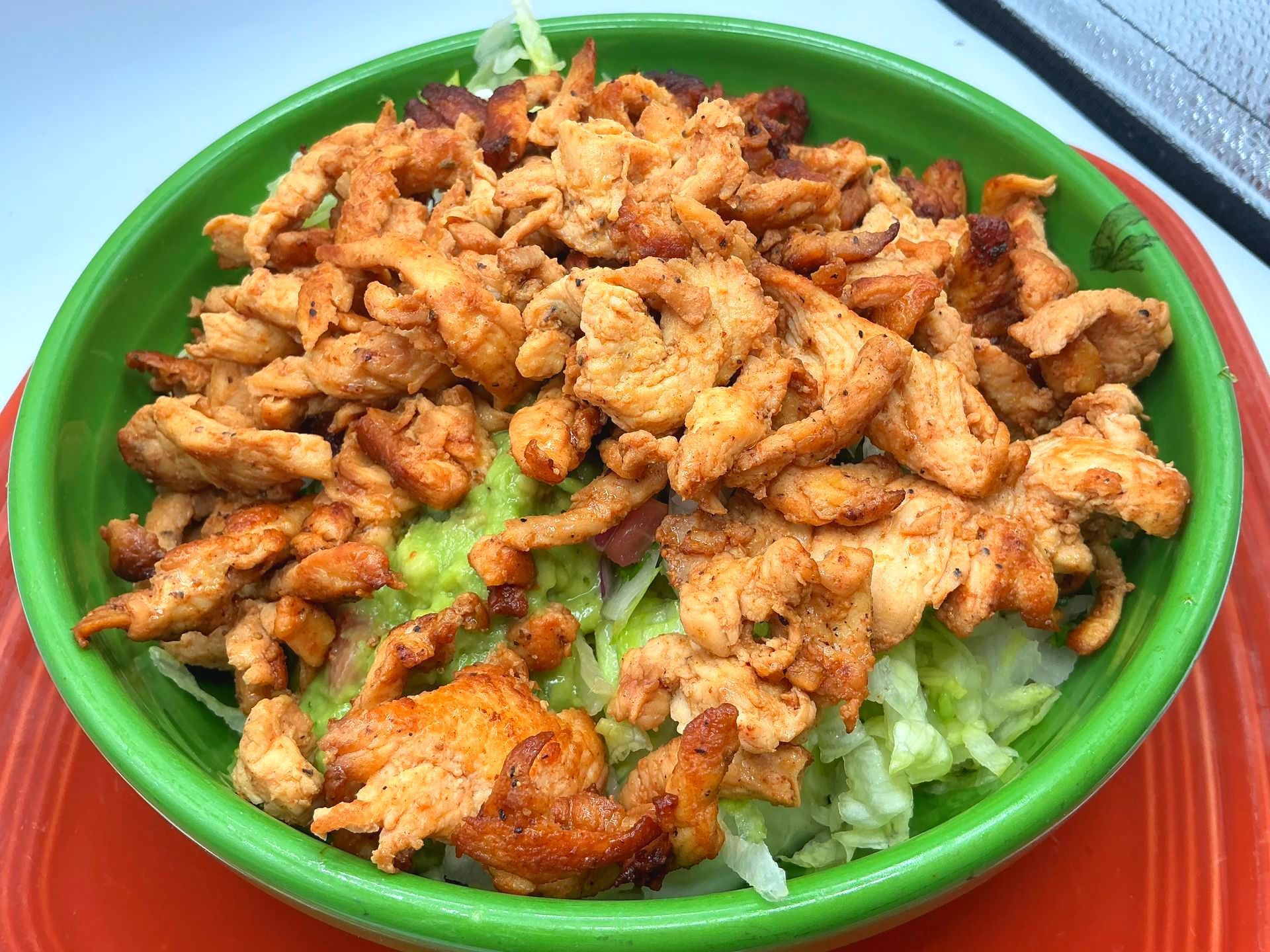 Chicken and guacamole salad in a green bowl, over lettuce on an orange plate.