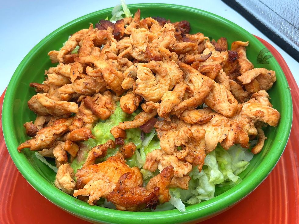 Chicken and guacamole salad in a green bowl, over lettuce on an orange plate.