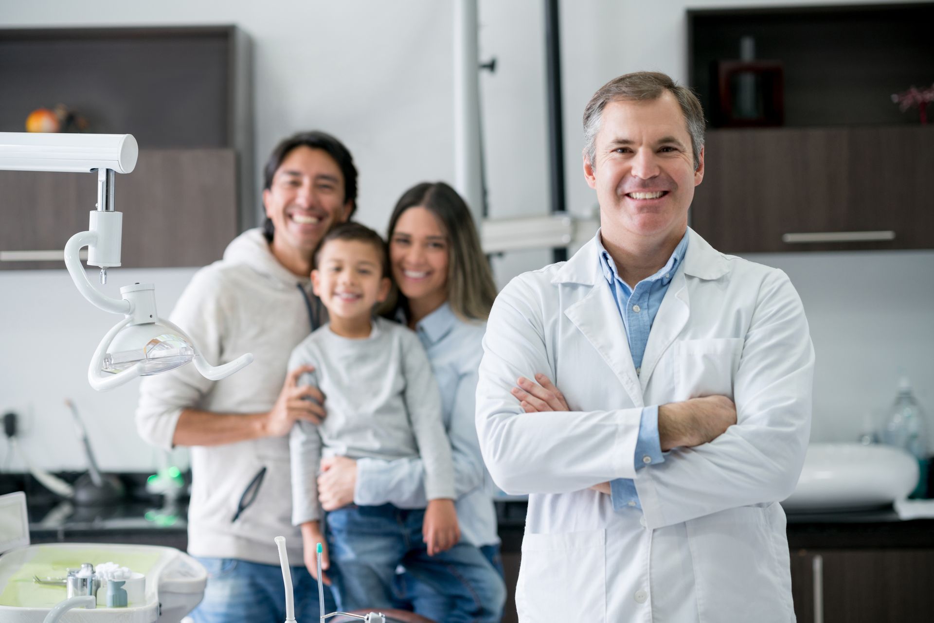 Happy dentist in office with smiling family in background, all looking cheerful.