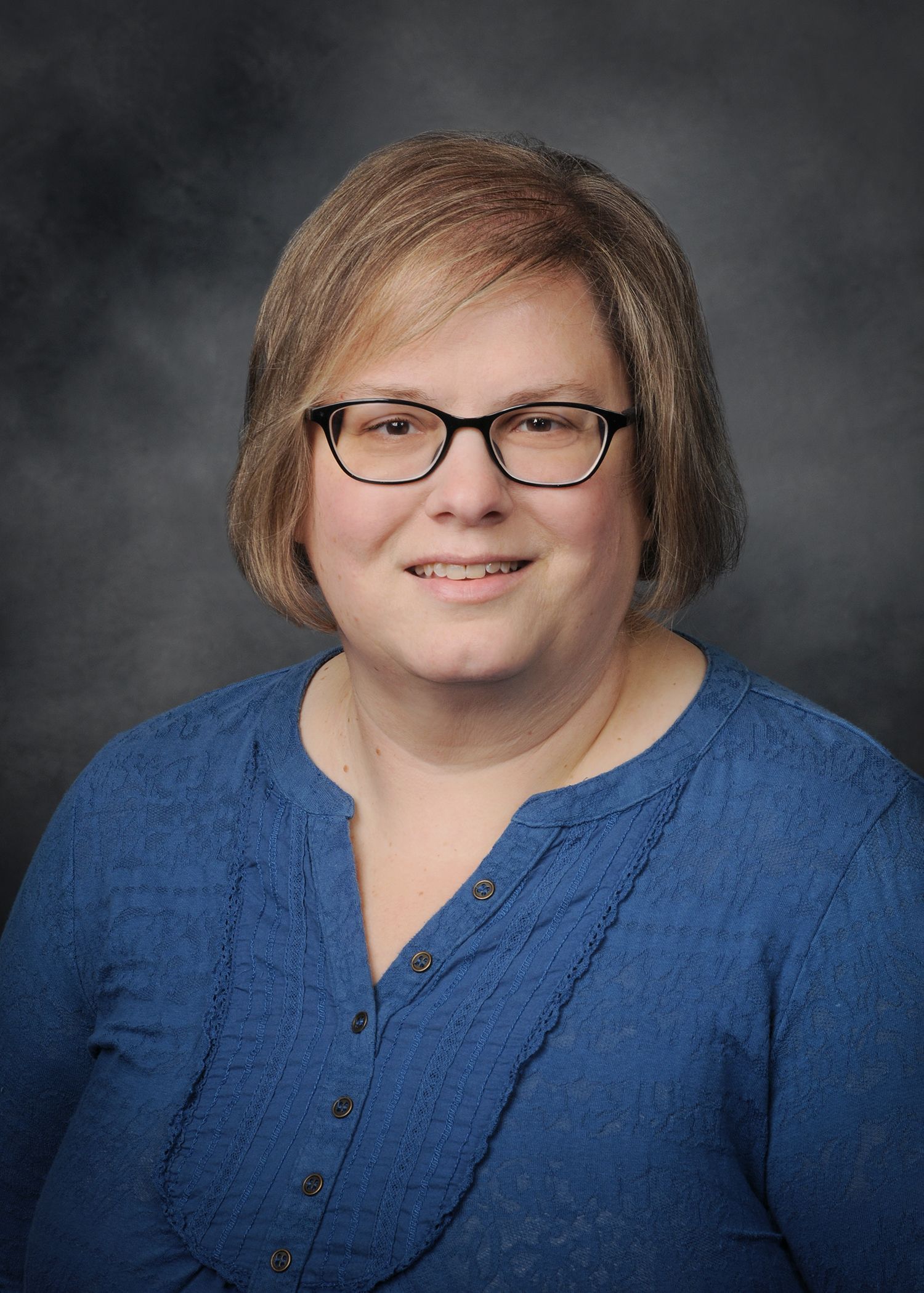 Portrait of a smiling person in a black cardigan and pink top against a gray studio background