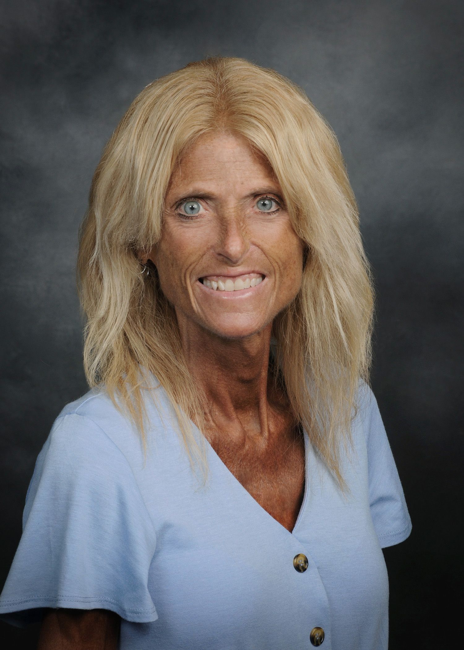 Portrait of a smiling person with blonde hair in a light blue shirt against a gray backdrop