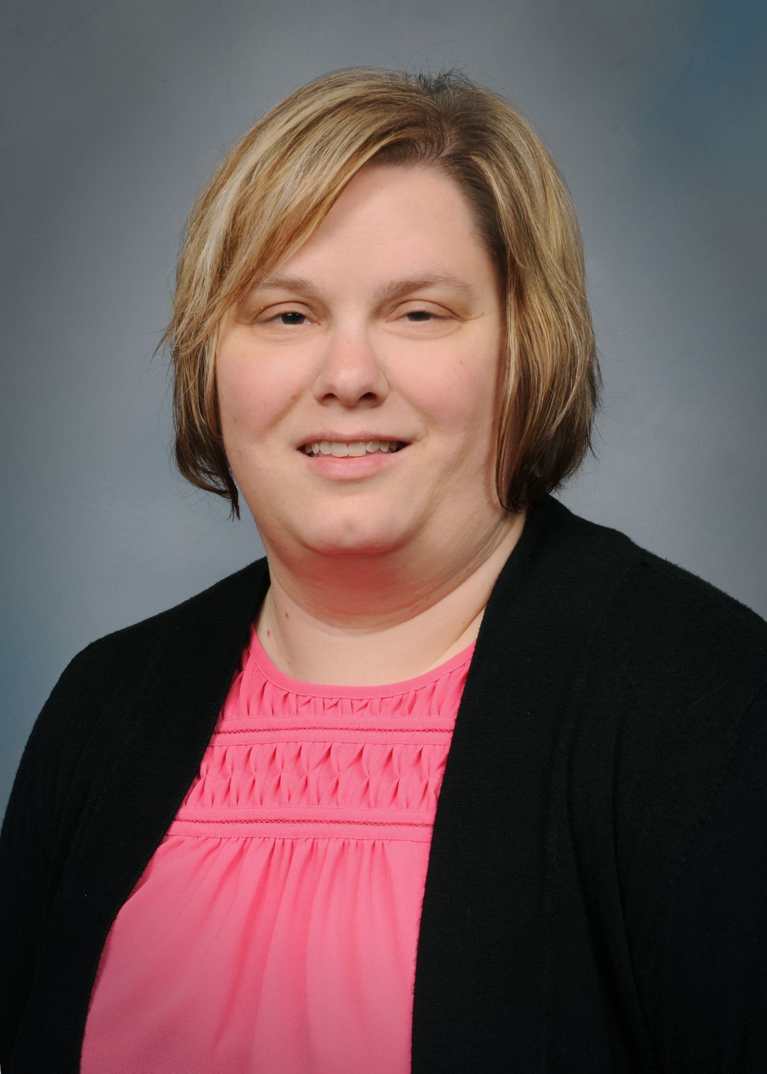 Portrait of a smiling person in a black cardigan and pink top against a gray studio background