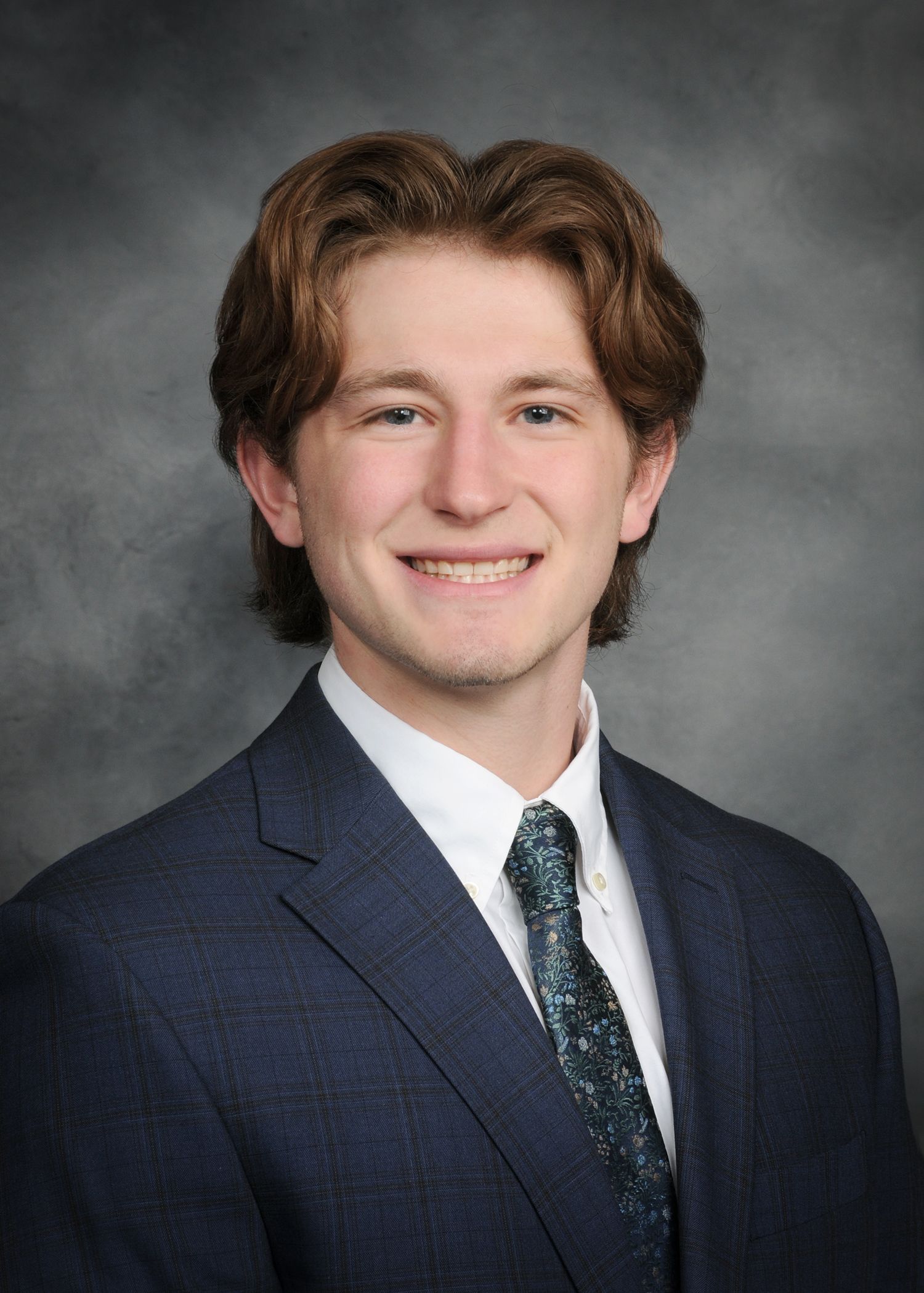 Smiling person in a navy suit and tie against a gray studio backdrop