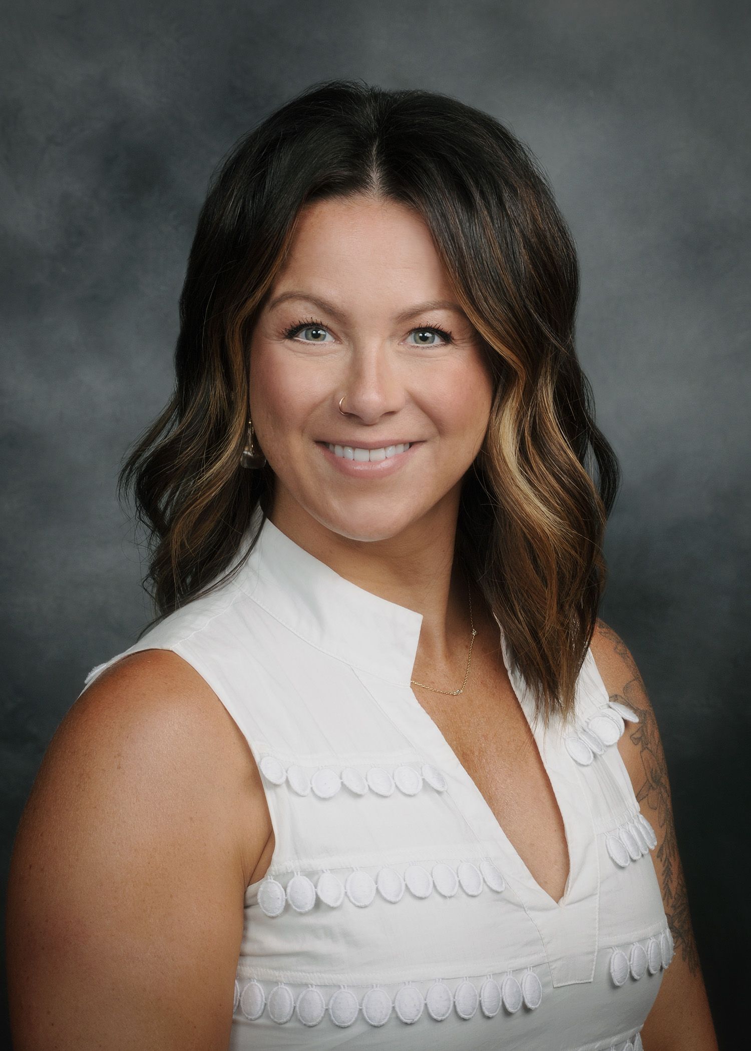 Portrait of a smiling woman in a white sleeveless blouse against a gray studio background