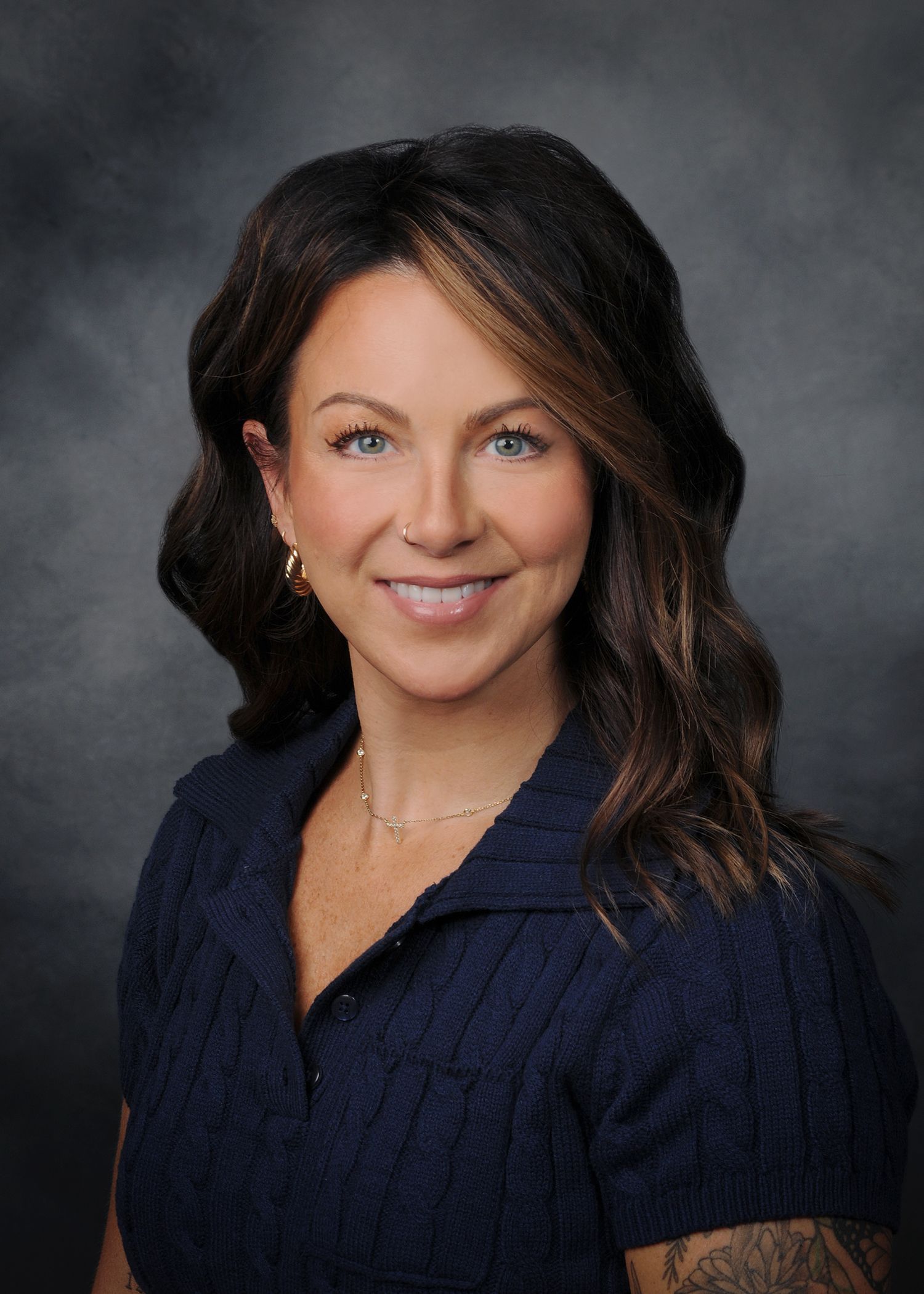 Portrait of a smiling woman in a white sleeveless blouse against a gray studio background