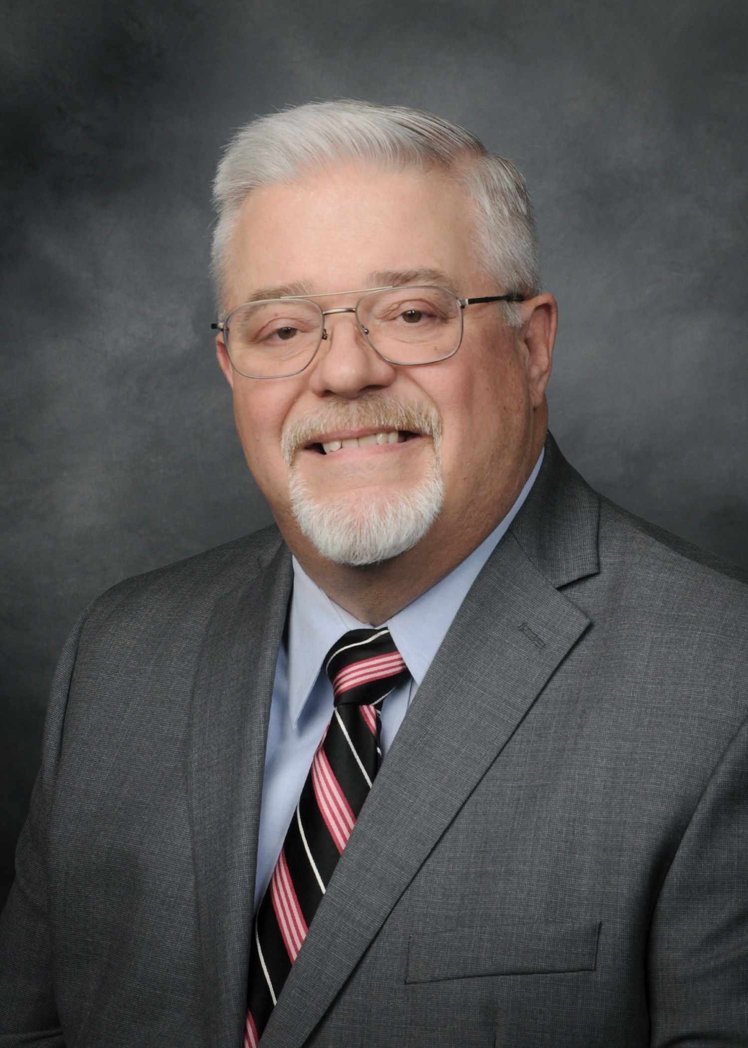 Smiling man in gray suit and pink striped tie against a gray studio backdrop