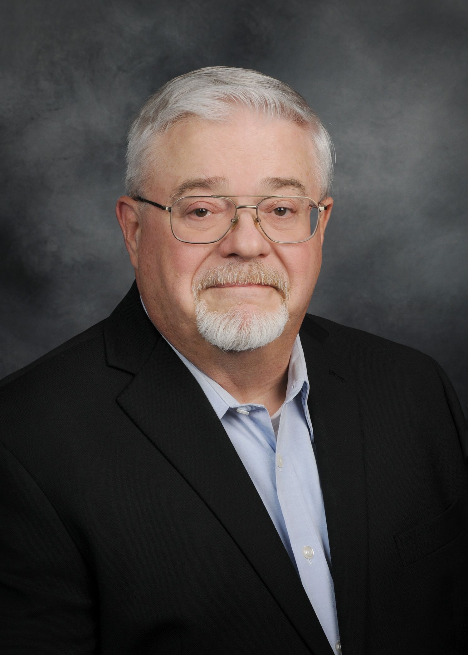 Smiling man in gray suit and pink striped tie against a gray studio backdrop