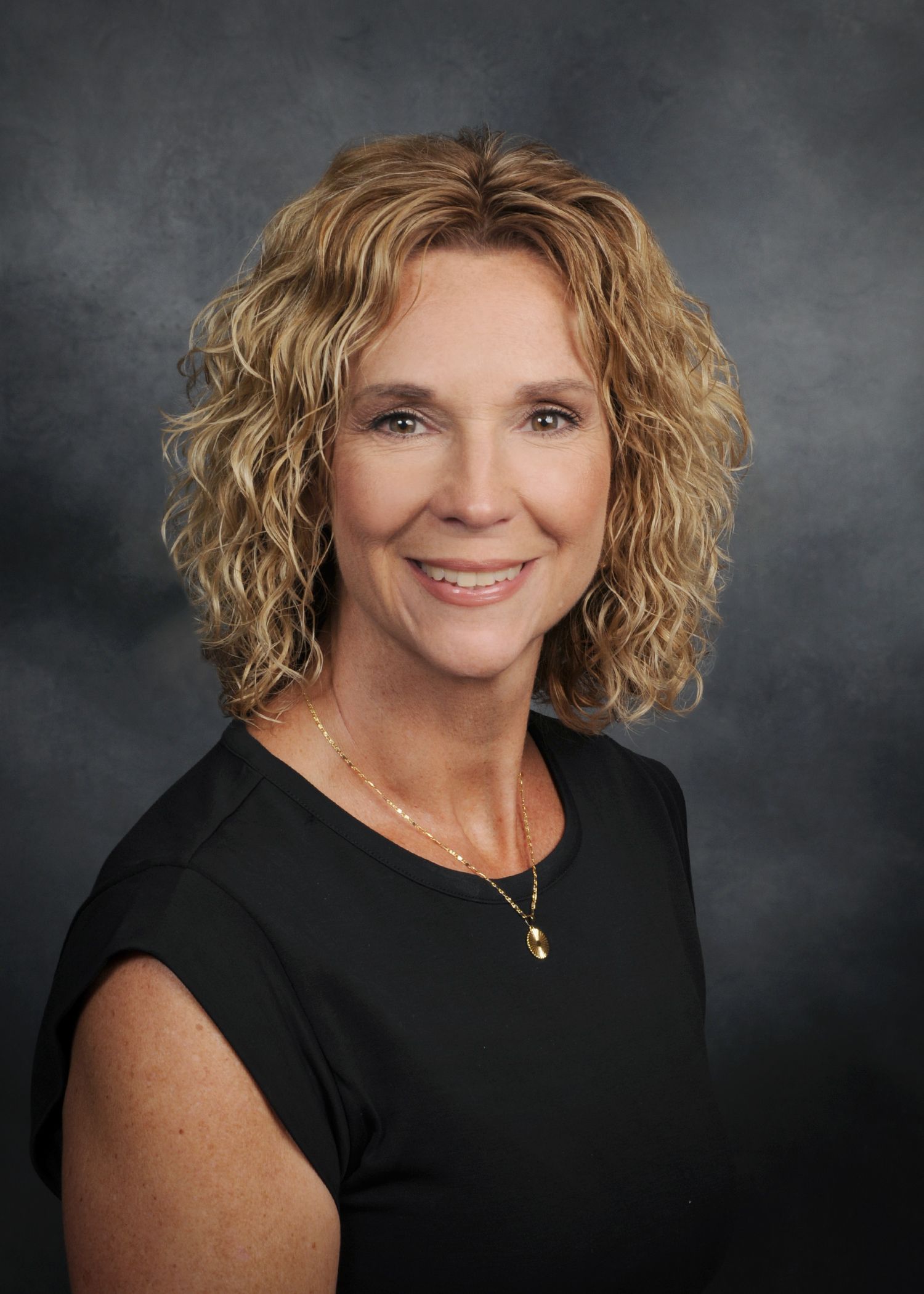 Portrait of a smiling woman with curly blonde hair in a white top against a gray backdrop