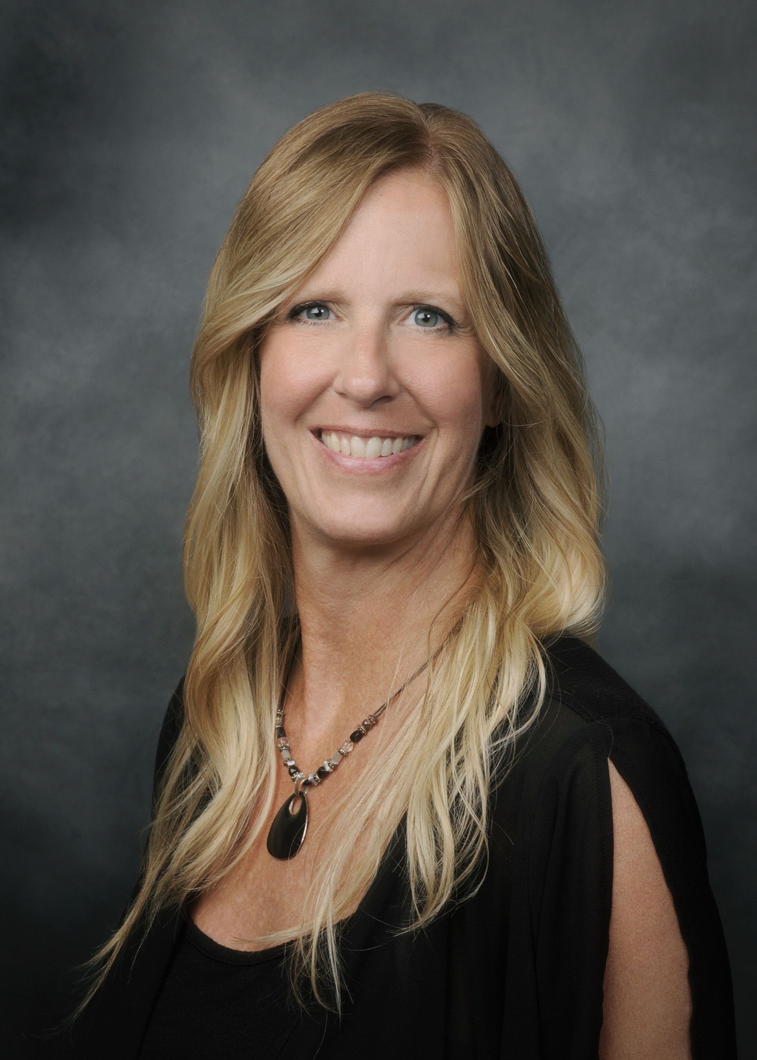 Smiling woman in a black top with long blonde hair against a gray studio background