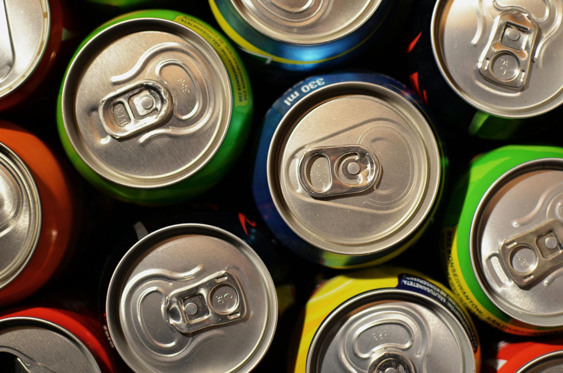 Overhead view of colorful soda cans, some open, some closed, arranged closely together.